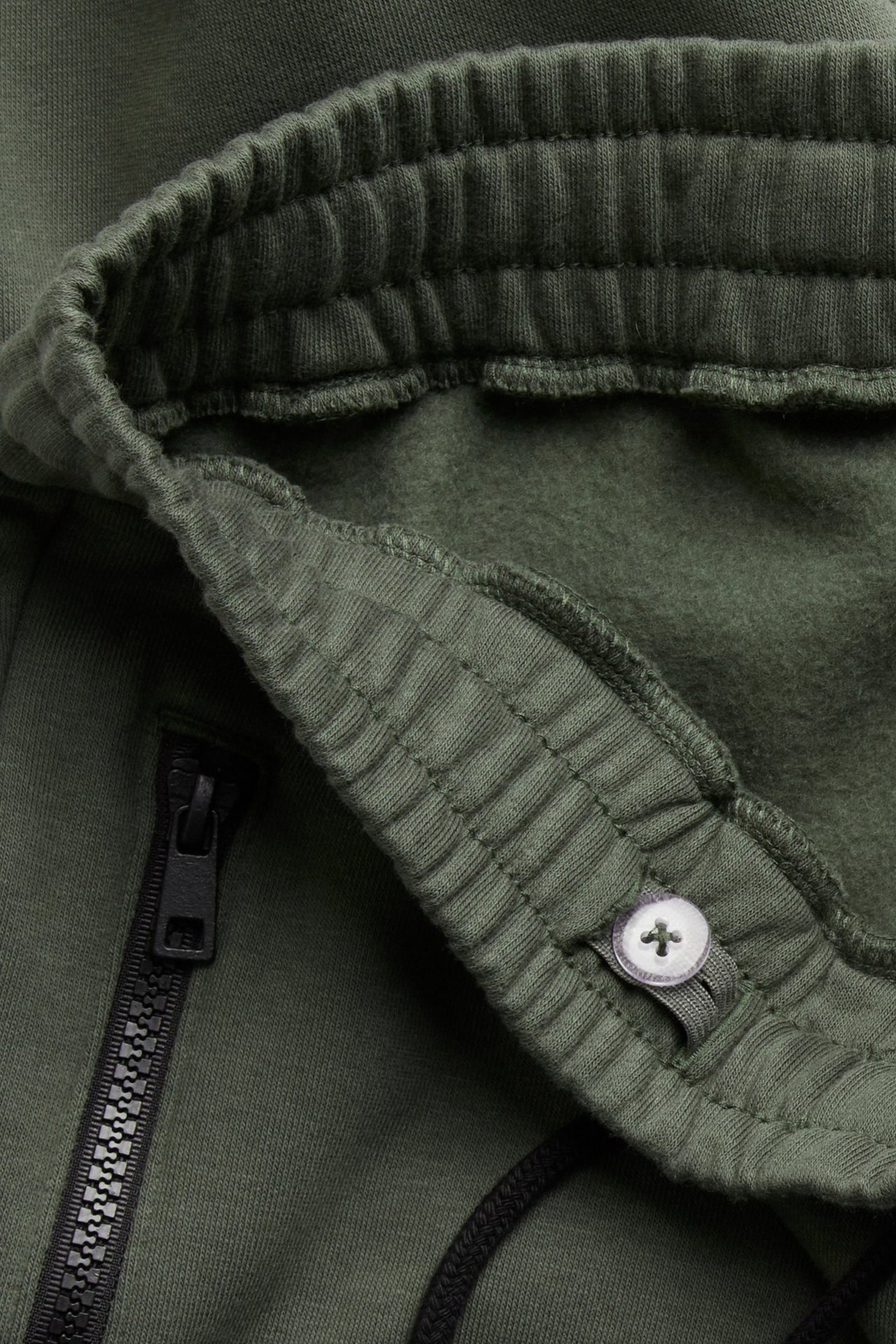 Zbliżenie zielonych bawełnianych spodni dresowych z elastyczną talią, czarnym sznurkiem i czarną kieszenią na zamek.