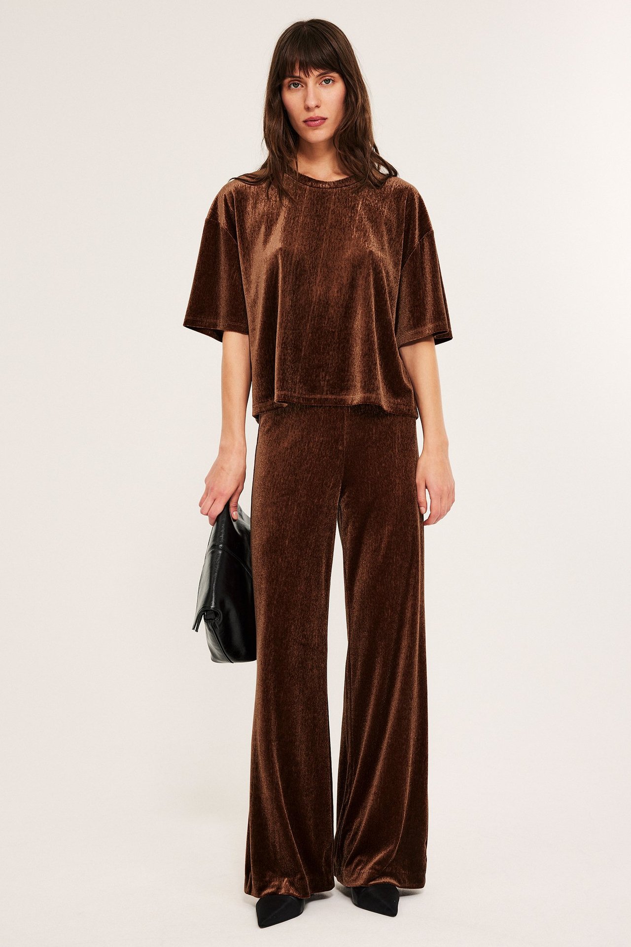 Kvinne i brune velourbyxor med brede ben, løs passform, T-skjorte.