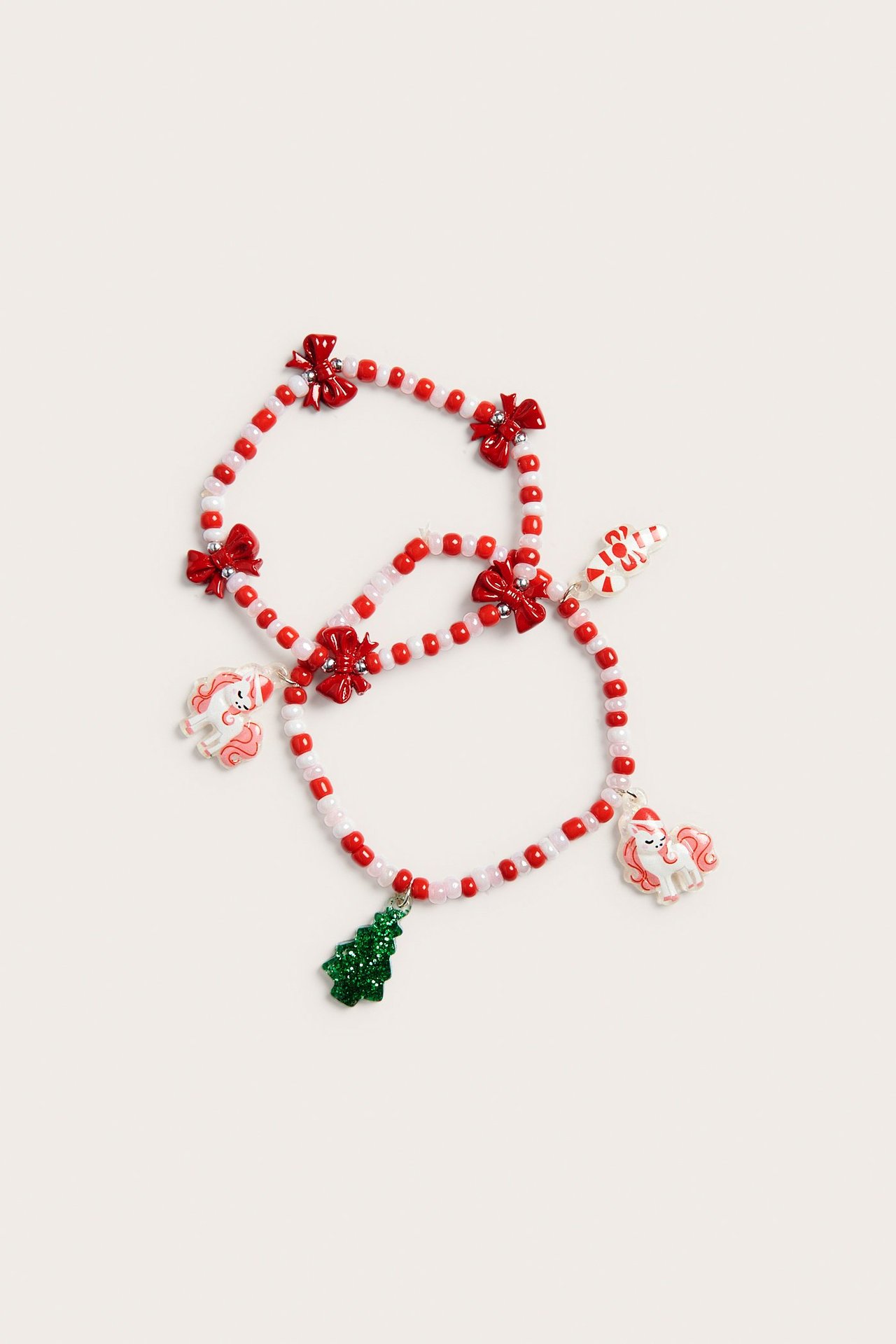 Widok z góry: dwie dziecięce czerwono-białe bransoletki z kokardkami, jednorożcami, choinką i cukrową laską.