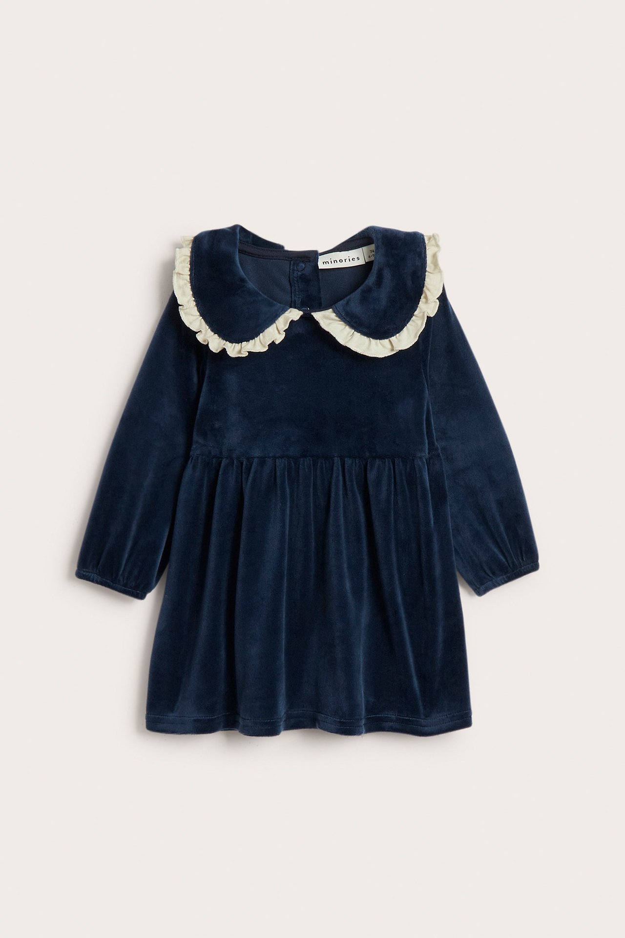 Frontvisning av en mørkeblå velour babykjole med lys volangkrage, lange ermer og knapping bak.