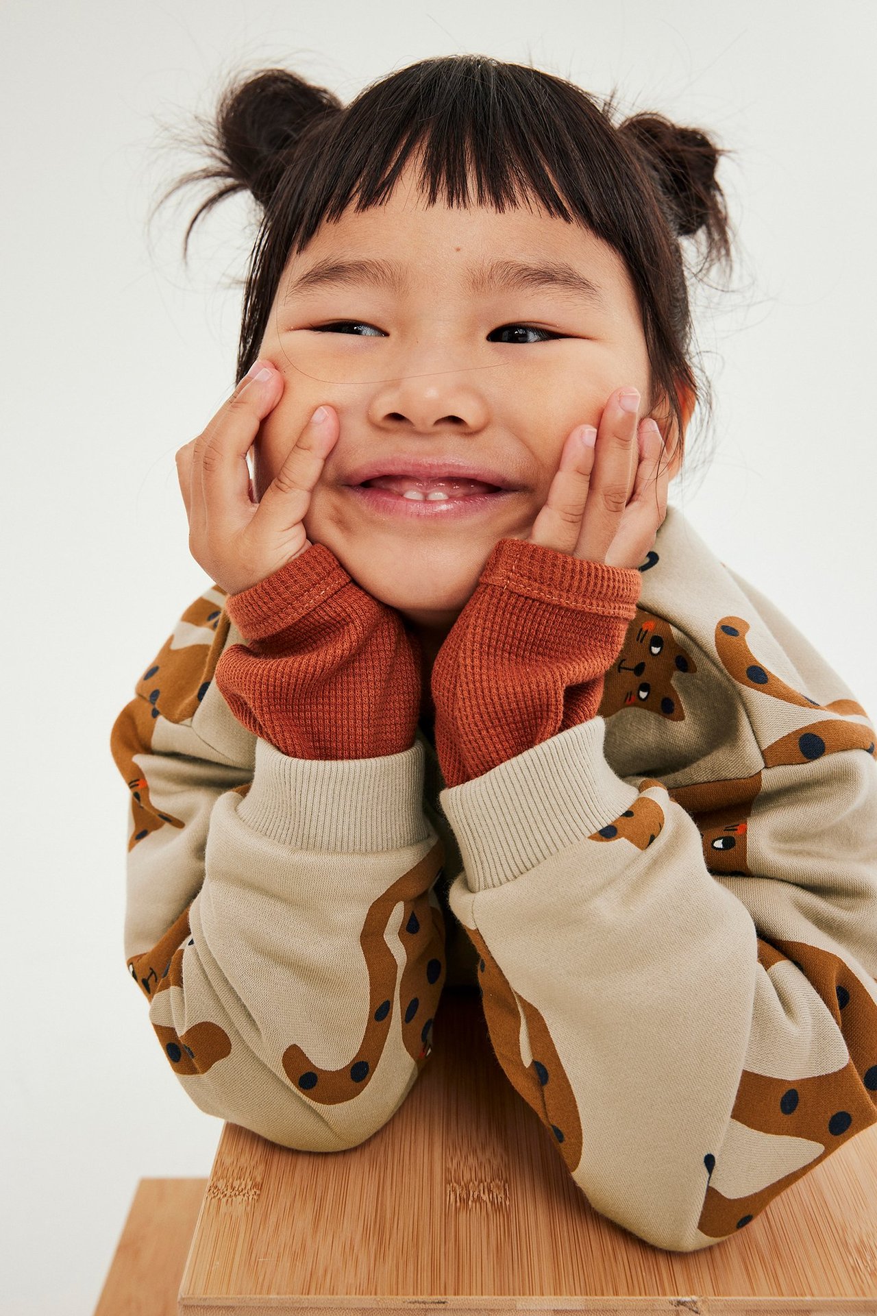 Barnunge i beige mønstret sweatshirt med print og røde mansjetter, smiler lykkelig.