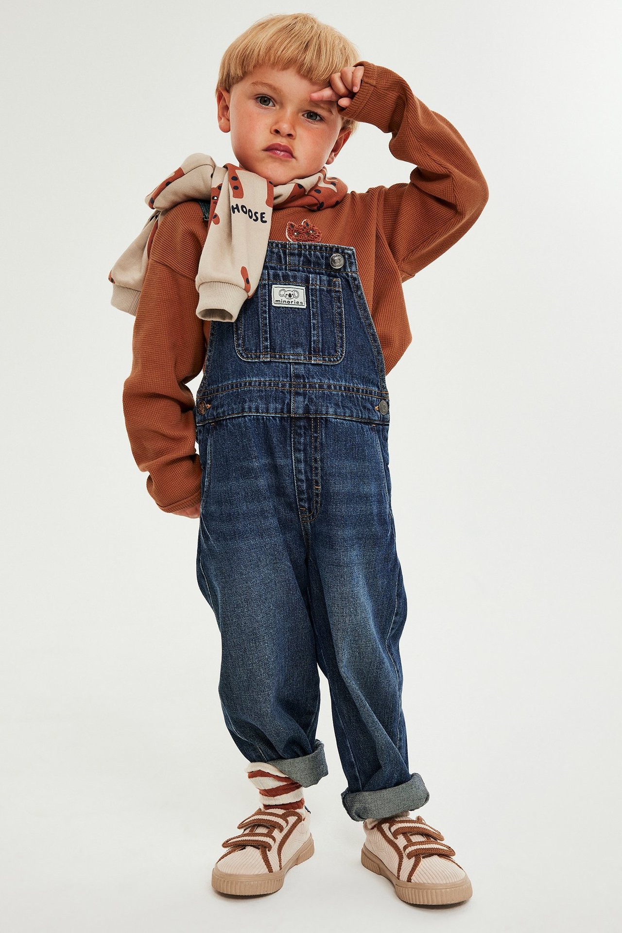 Barn i brunt långärmad top i våffelkvalité med brodyr på bröstet, jeans och sneakers.