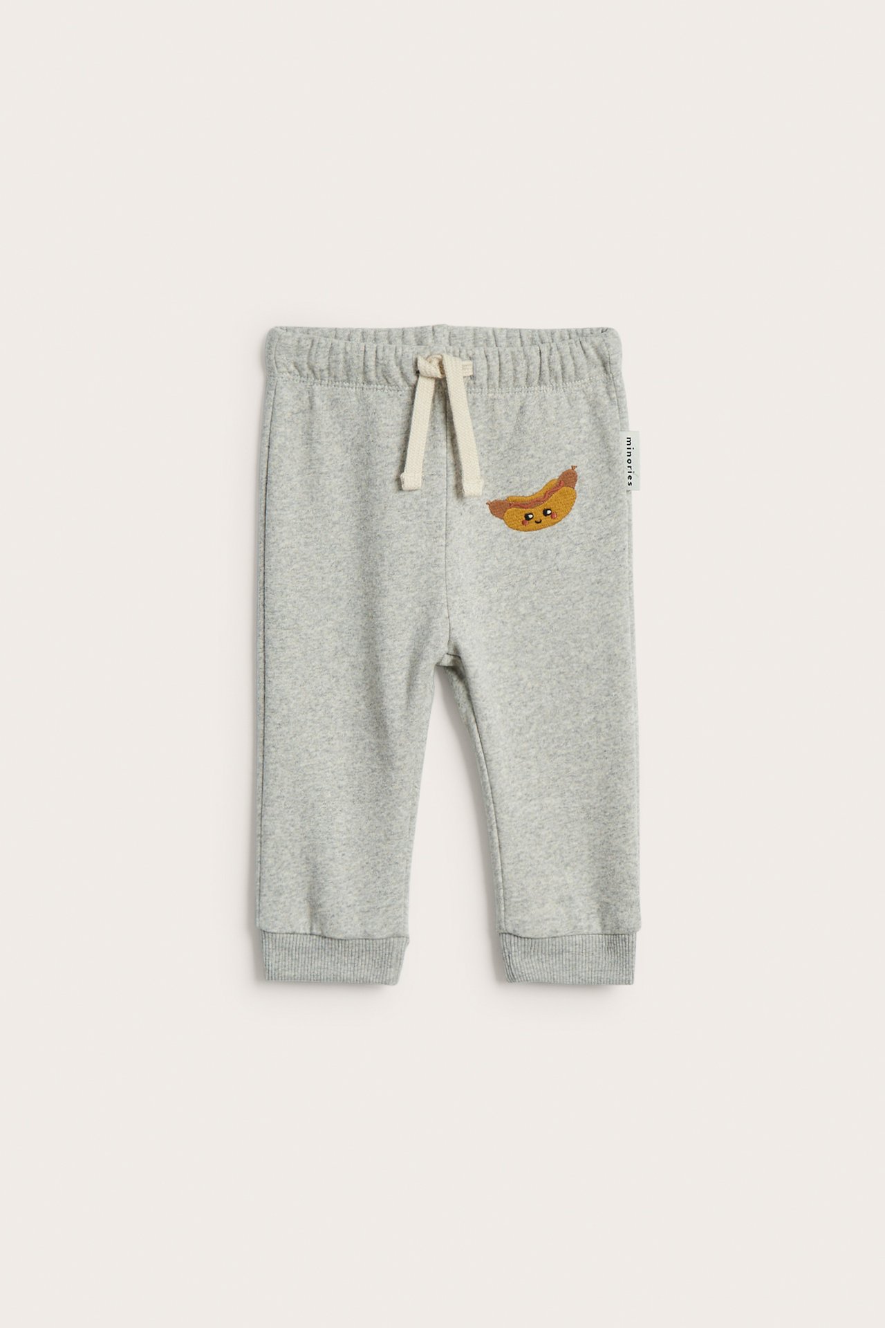 Frontvisning av lysegrå babyjoggebukse i bomullsblanding med pølsebroderi og snøring.
