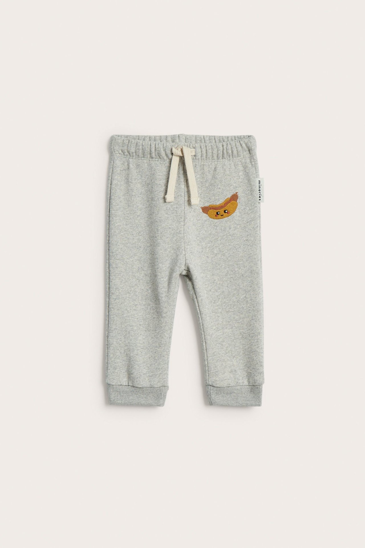 Frontvy av ljusgrå babyjoggingbyxor i bomullsmix med broderad korv och dragsko.