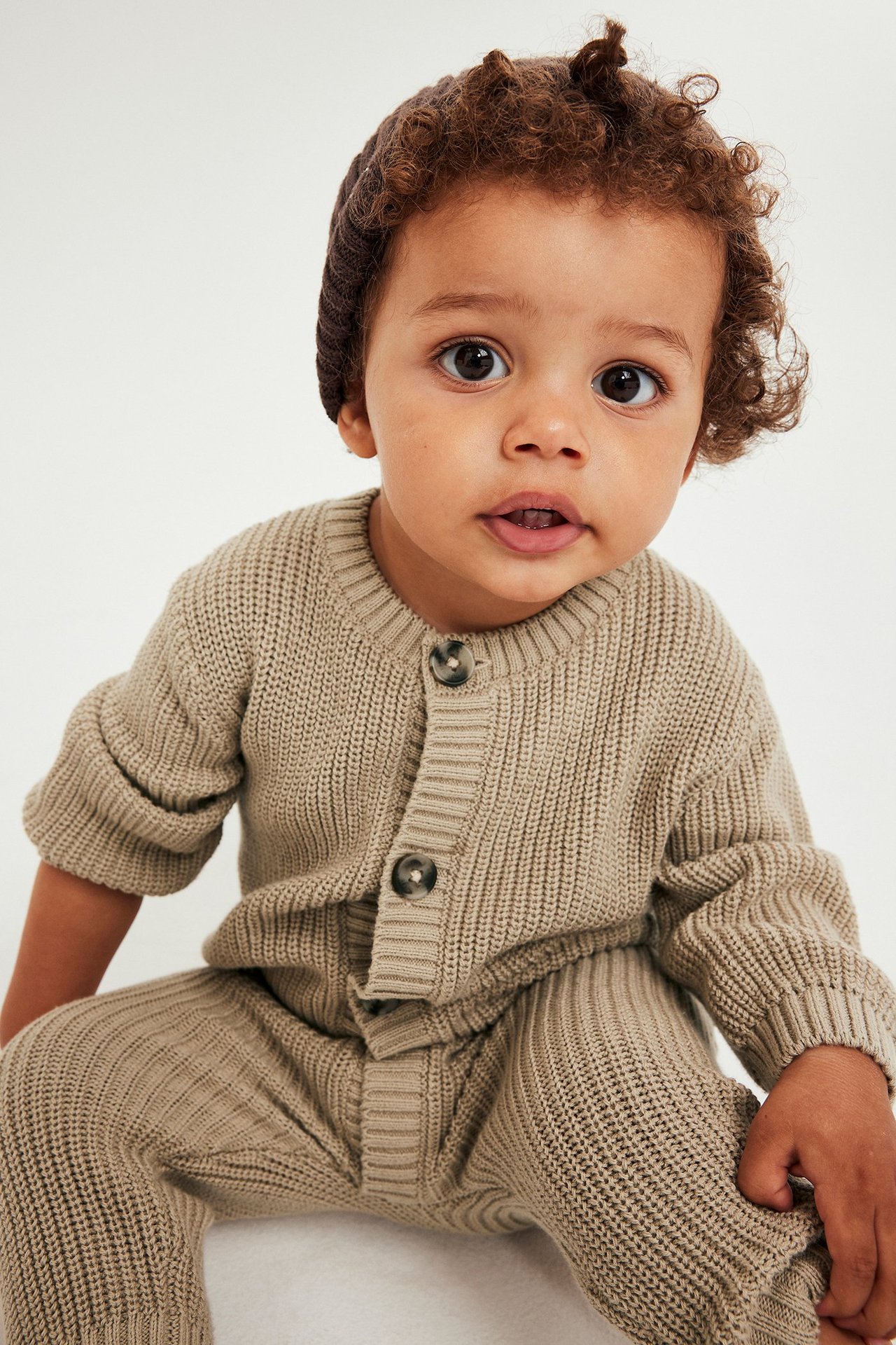 Beige neulottu vauvan haalari etupainikkeilla, 100 % puuvillaa, yksivärinen.