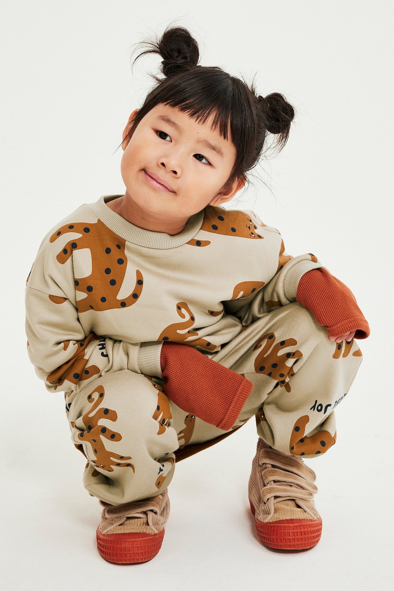 Mała dziewczynka w beżowych dżinsach z nadrukiem zwierząt, kieszenie, regulowany pas i ściągacze.