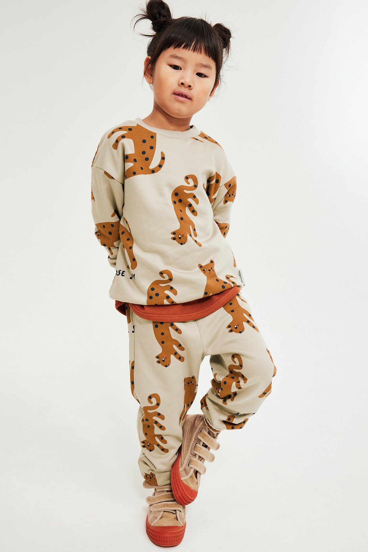Dziewczynka w beżowych spodniach dresowych z dinozaurami, kieszeniami i siateczką.