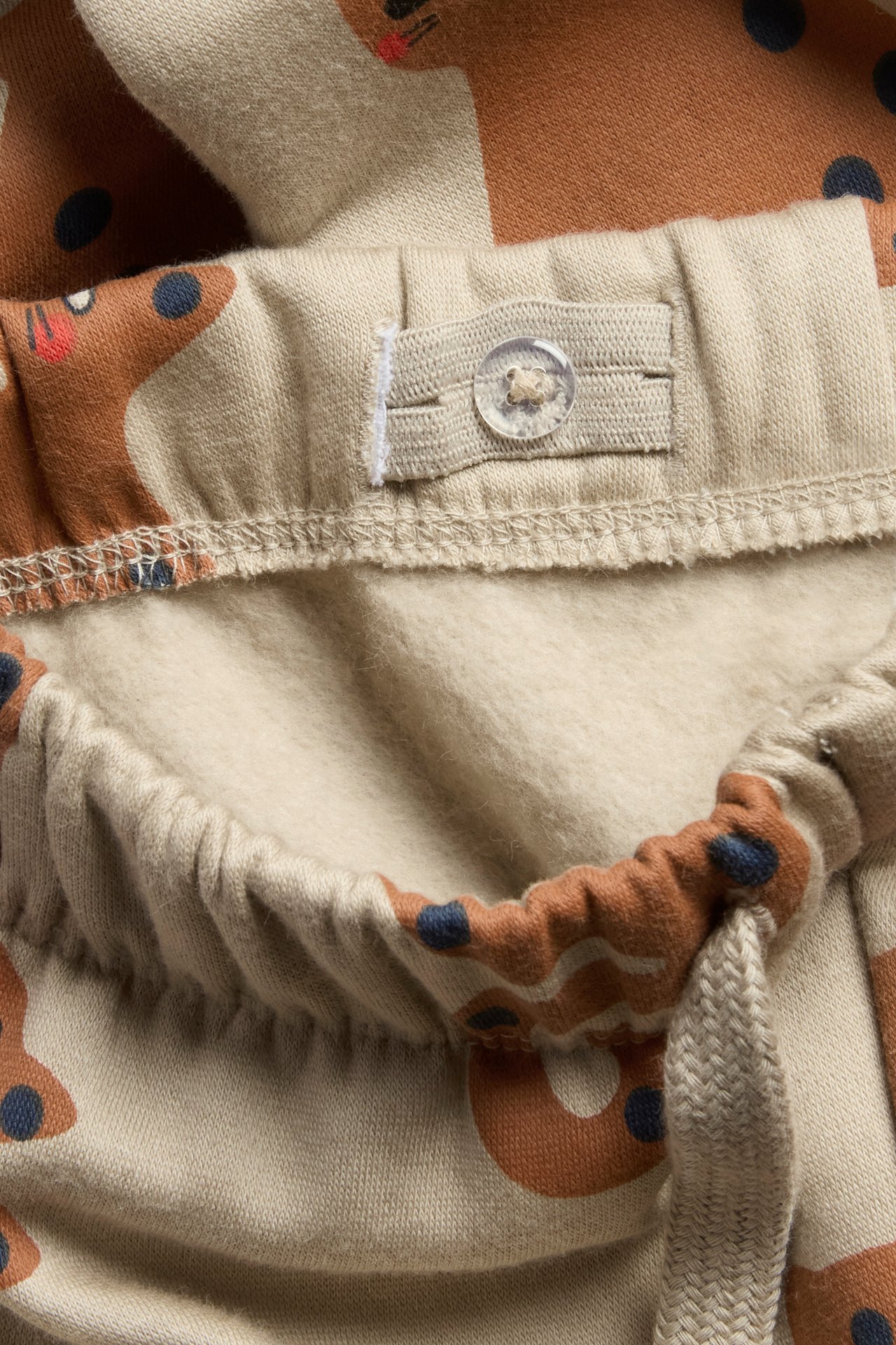 Beżowe dżinsy z nadrukiem, kieszenie boczne, regulowany pas, ściągacze na końcach.