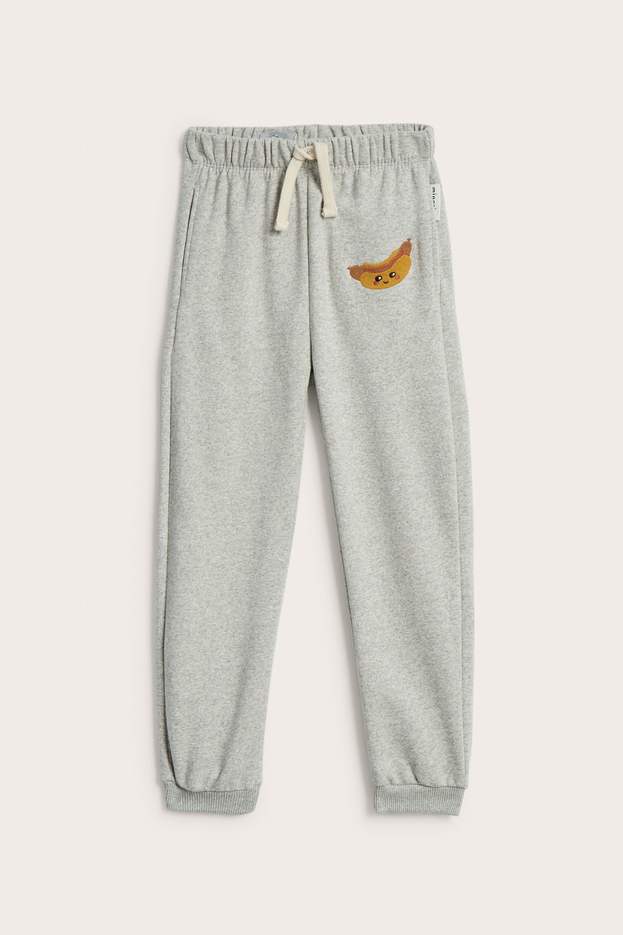 Front: Lysegrå joggebukse for barn med strikk i midjen, snøring, ribbekanter og pølsebroderi.