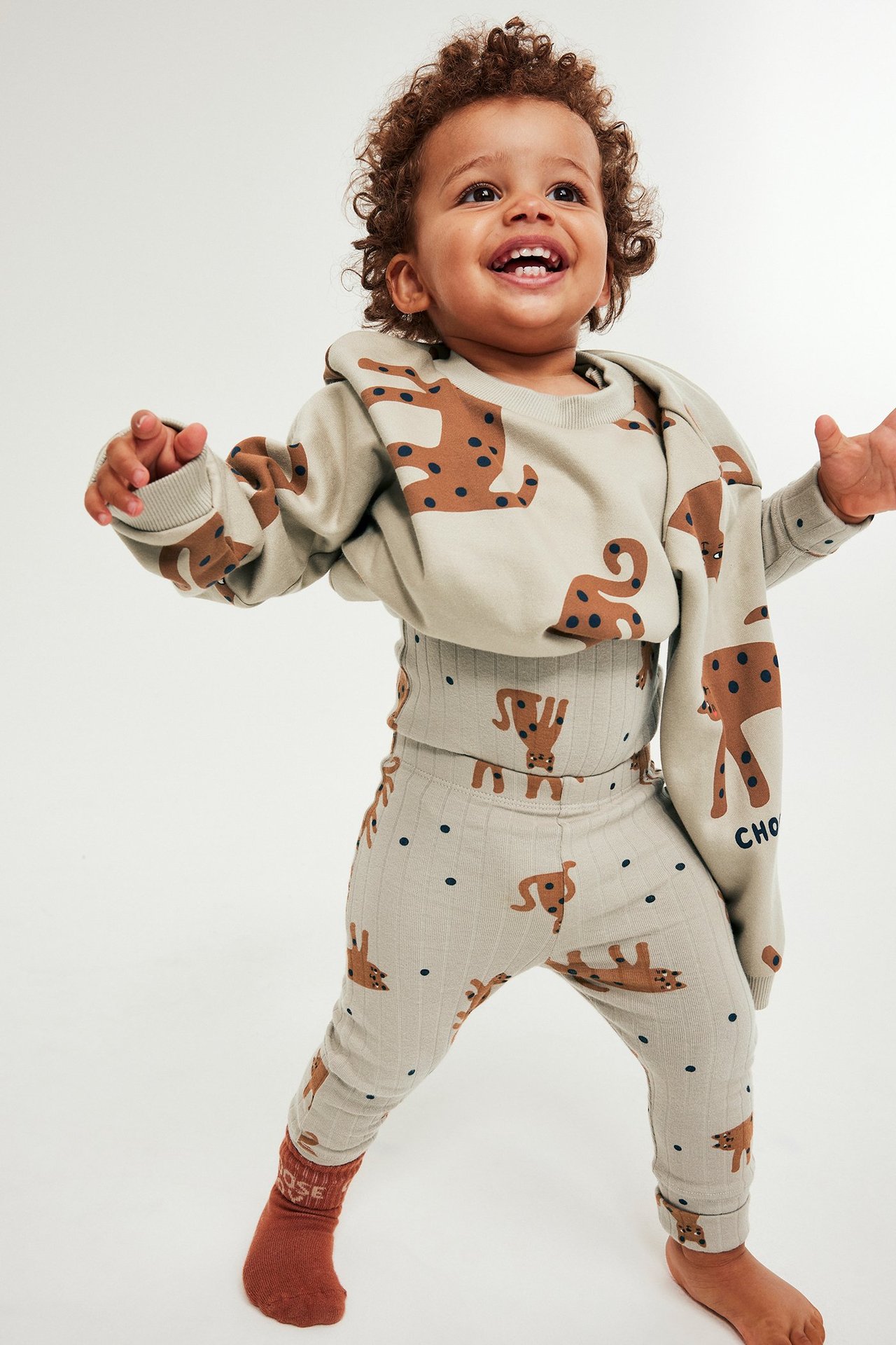 Iloinen vauva beigestä eläinprinttileggingsistä, yllään paita, huppari ja sukat.