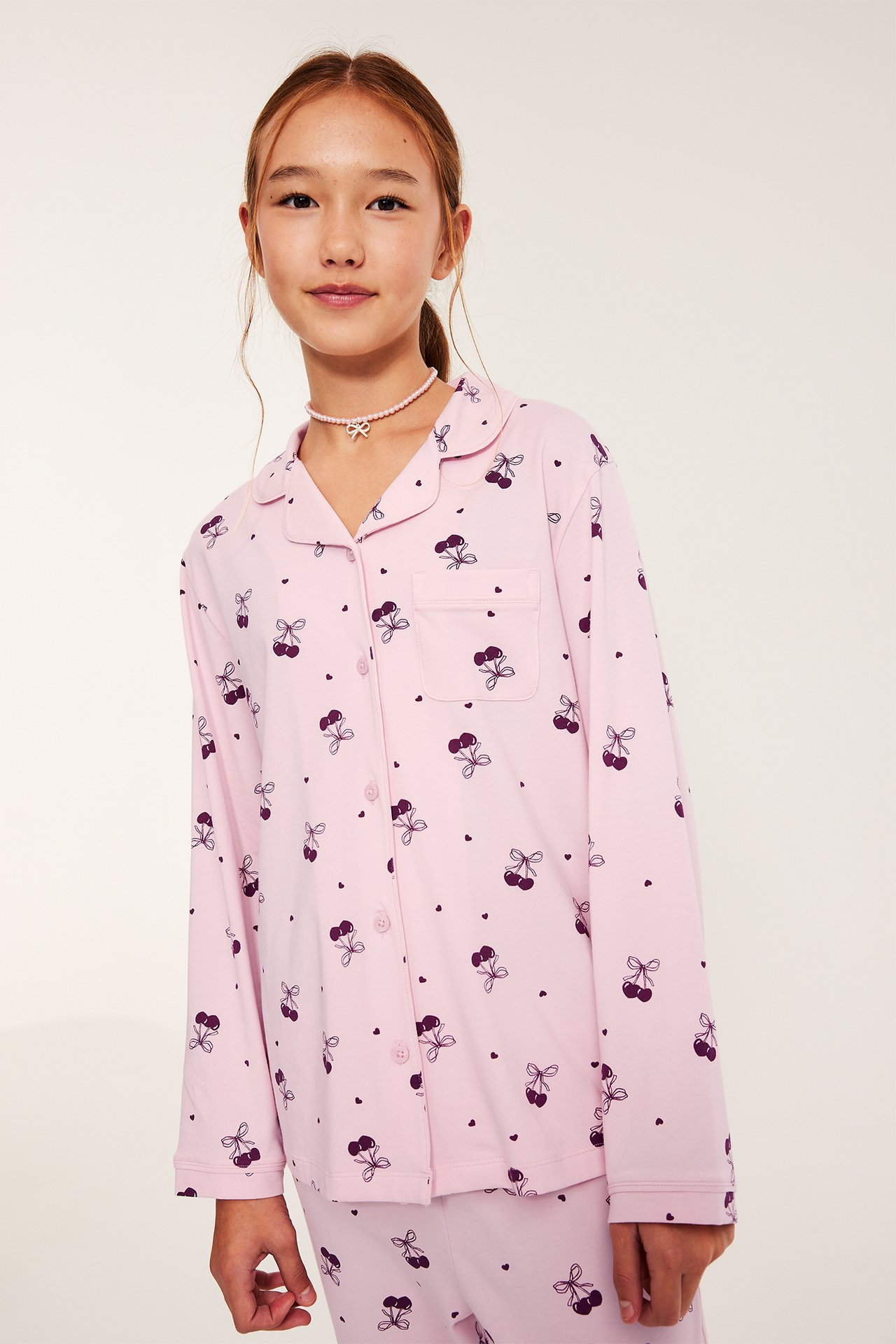 Tyttö vaaleanpunaisessa trikoota pajamaas, napit edessä, kirsikkamainen kuvio.