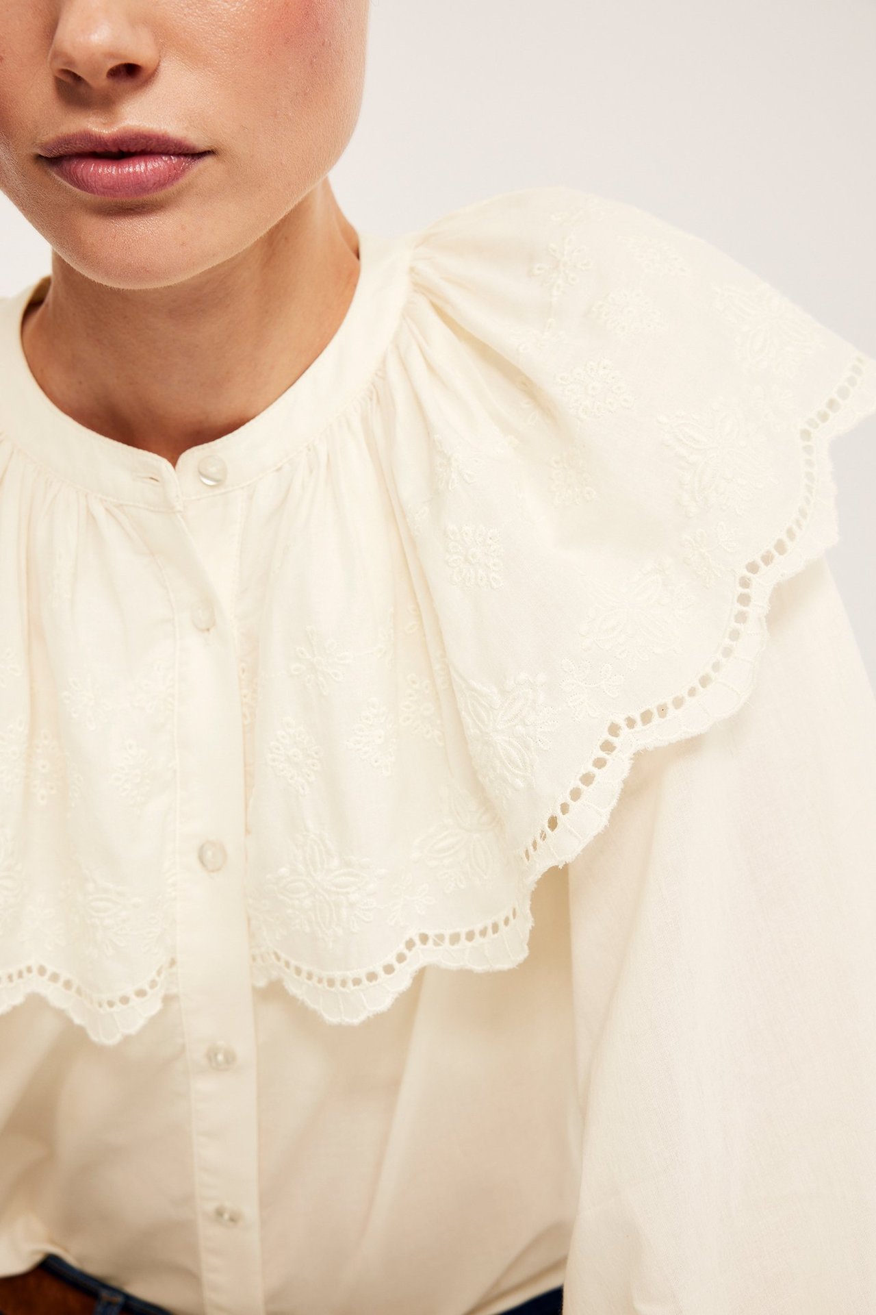 Lähikuva naisesta yllään luonnonvalkoinen puuvillapusero brodeeratulla kaulukapella ja napeilla edessä.