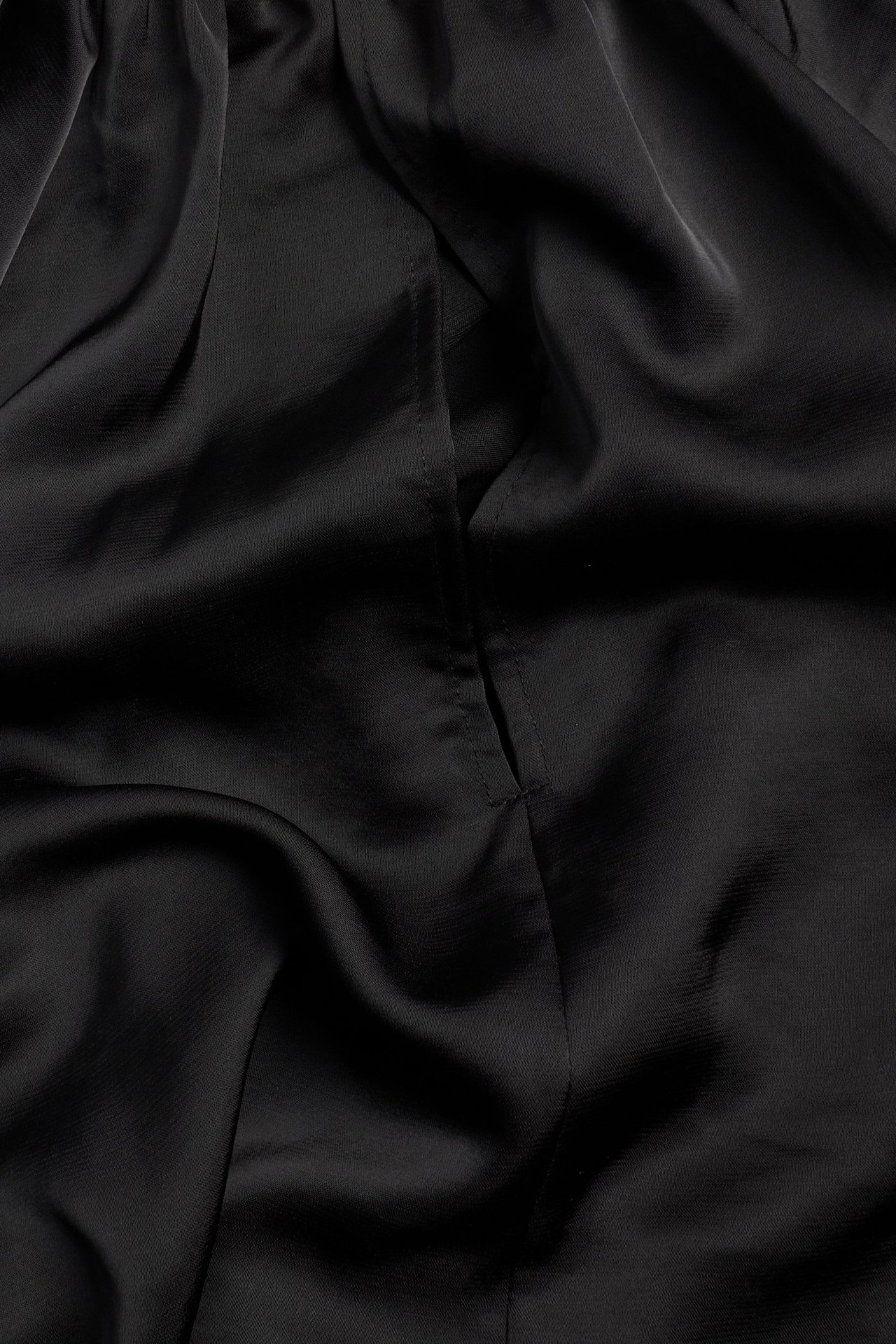 Zbliżenie czarnej tkaniny bluzki poliestrowej, ukazujące jej udrapowaną fakturę i subtelny szew.