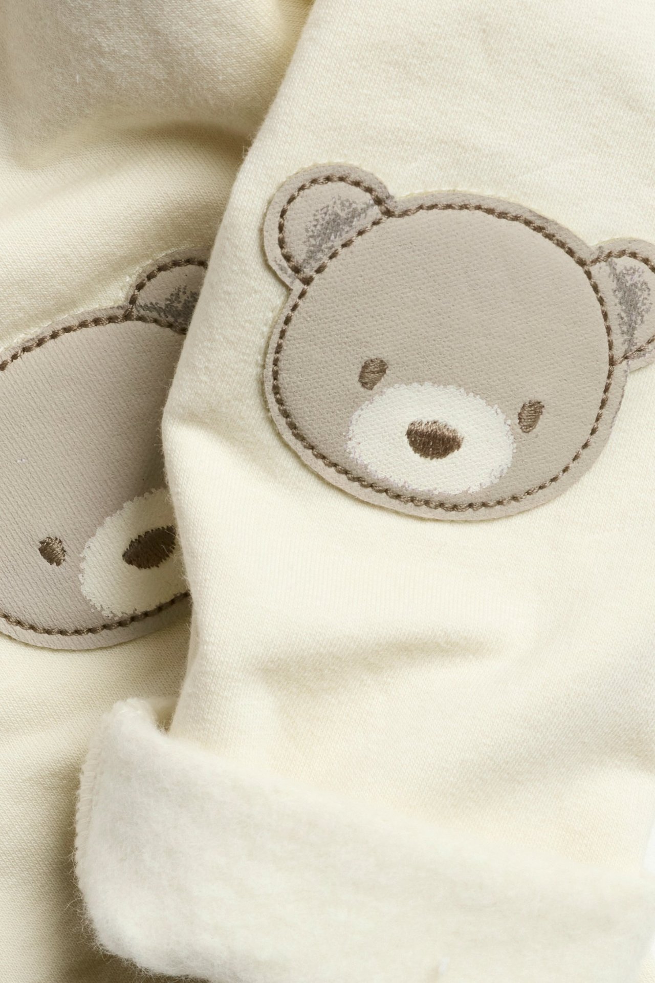 Zbliżenie na jasnobeżowe legginsy niemowlęce z szarymi aplikacjami misia na kolanach.