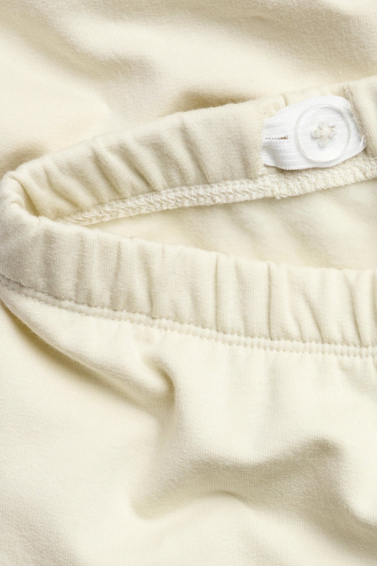 Zbliżenie jasnobeżowych bawełnianych legginsów z regulowaną gumką w pasie i białym guzikiem.