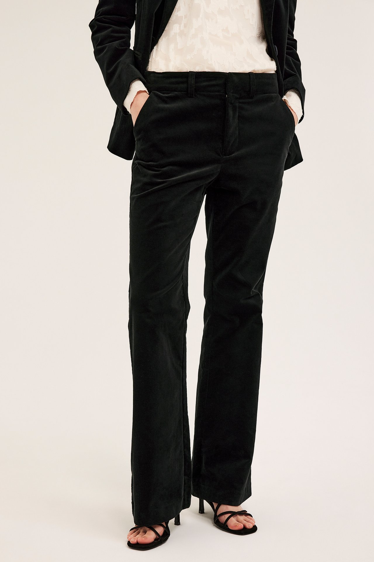 Edestä, nainen yllään mustat suorat samettihousut, musta samettibleiseri, valkoinen toppi ja mustat korkosandaalit.