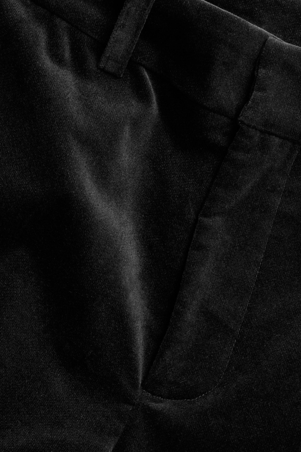 Zbliżenie czarnych jednolitych aksamitnych spodni, widać kieszeń i szlufkę na pasek.