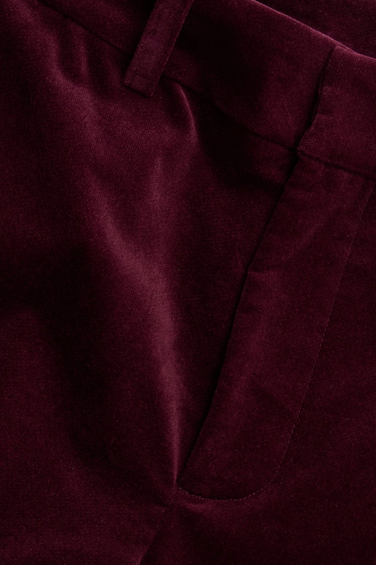 Zbliżenie na bordowe aksamitne spodnie, pokazujące kieszeń i szlufkę.