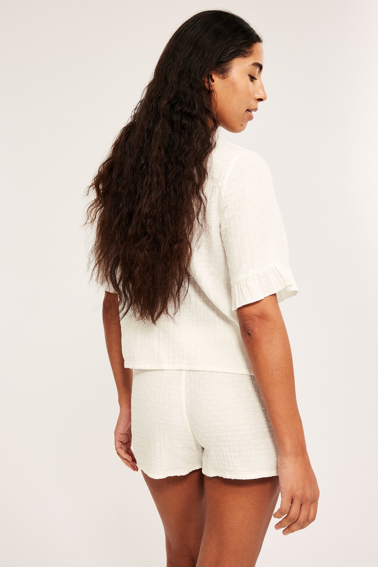 Naisen sivukuva off-white kuvioidussa puuvillapyjamasetti: röyhelöhihainen toppi ja shortsit.