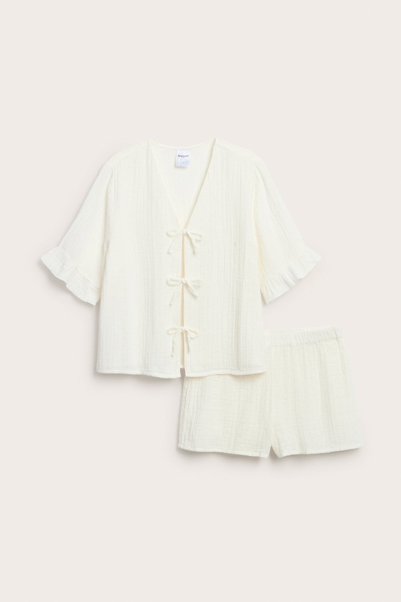 Widok z przodu: kremowa piżama bawełniana. Top z kokardkami, marszczonymi rękawami i szorty.