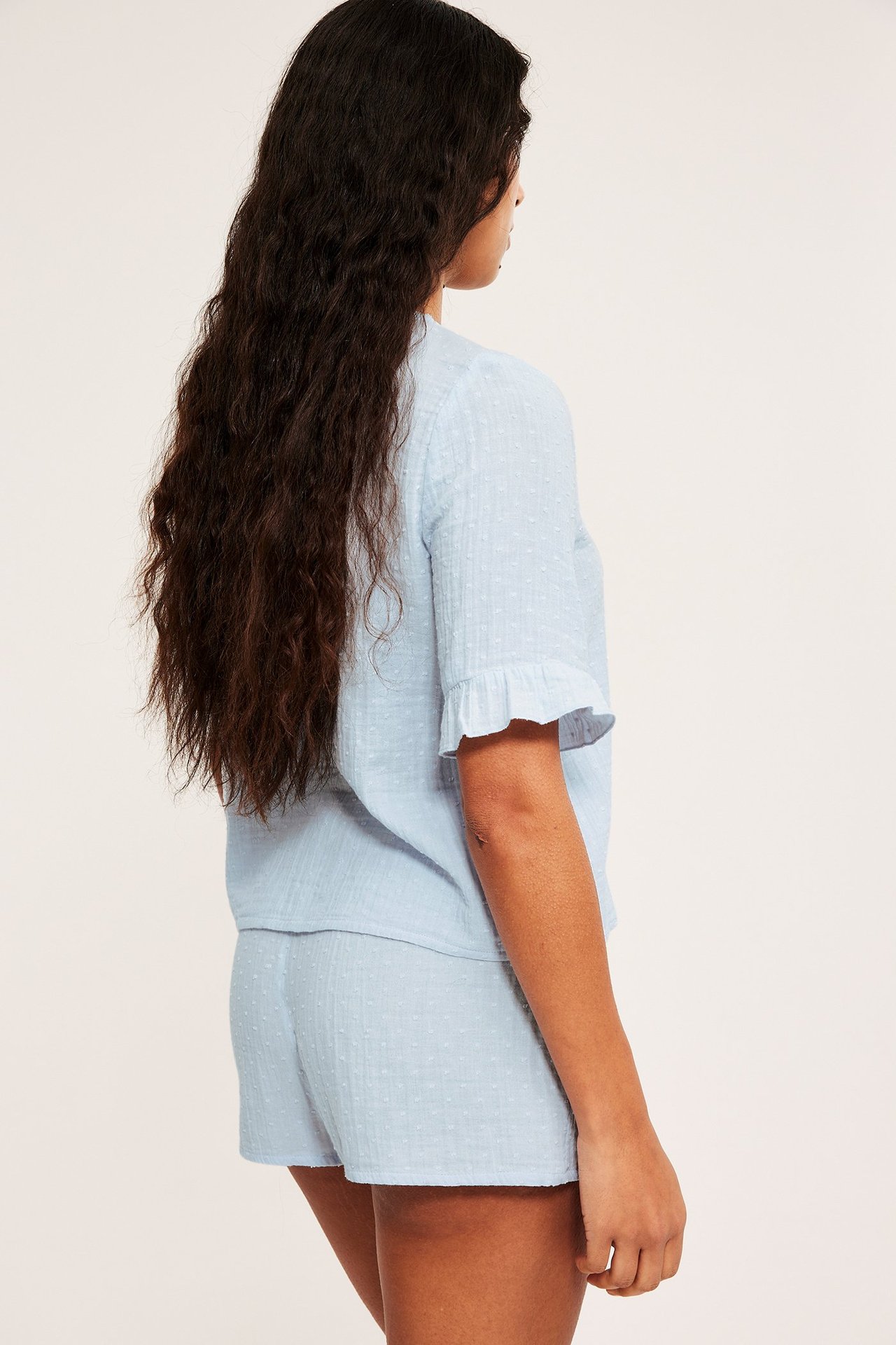 Sivukuva naisesta yllään vaaleansiniset puuvillapyjamat, joissa lyhythihainen röyhelöpaita ja yhteensopivat shortsit.