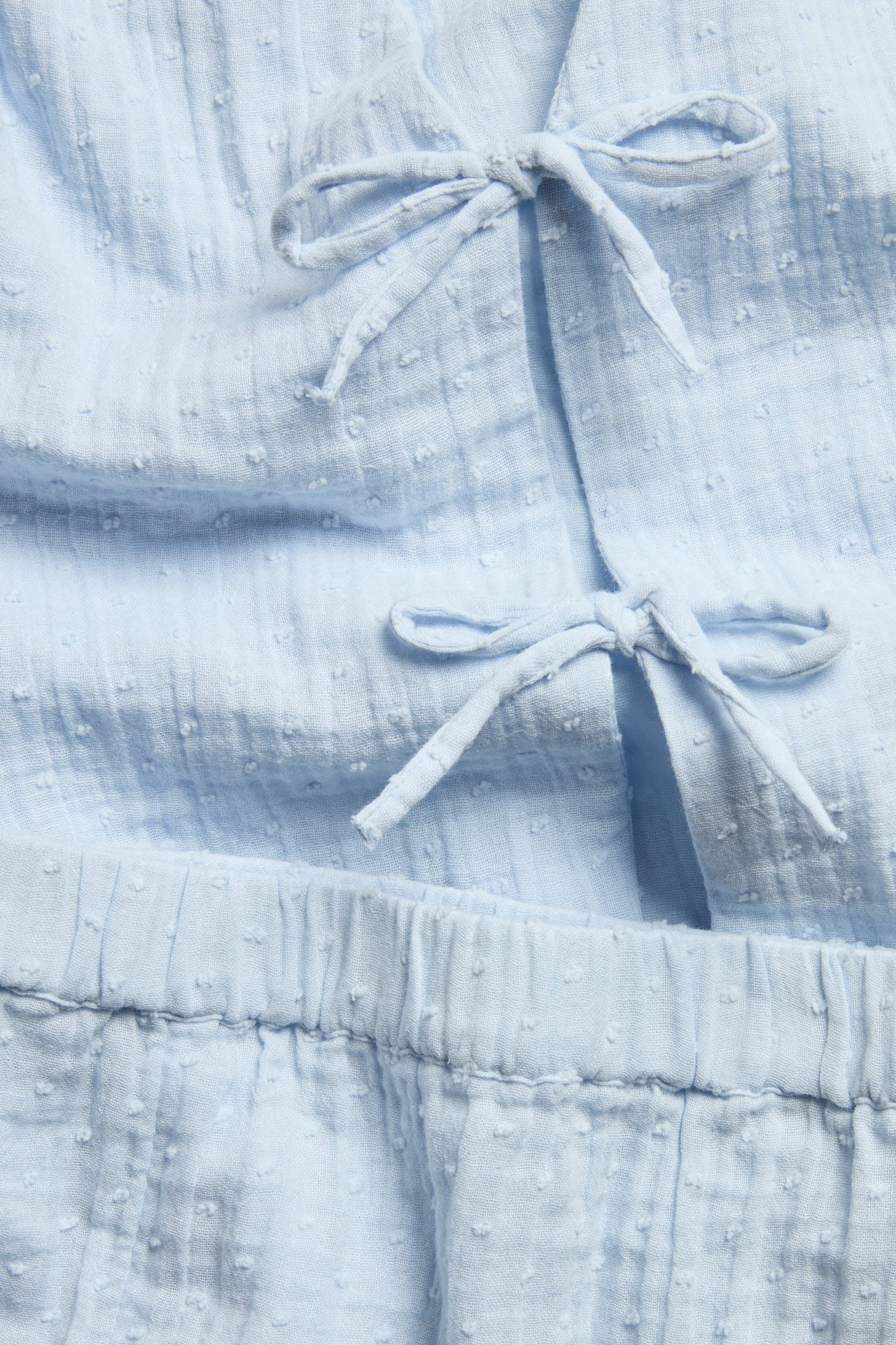 Zbliżenie na jasnoniebieską bawełnianą piżamę w kropki, z wiązaniami u góry i elastyczną talią.