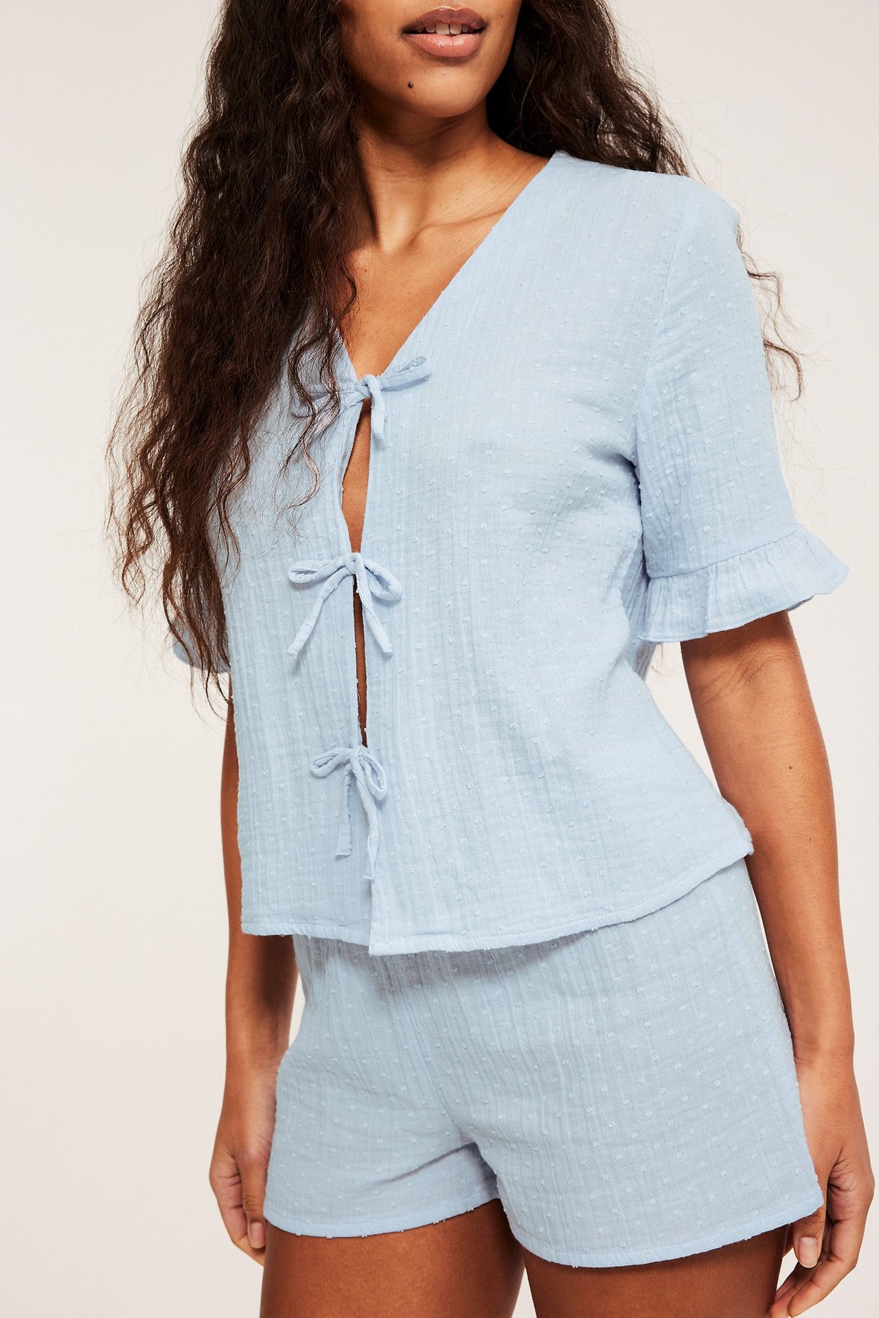 Widok z przodu: kobieta w jasnoniebieskiej bawełnianej piżamie, wiązana góra z falbankami, pasujące szorty.