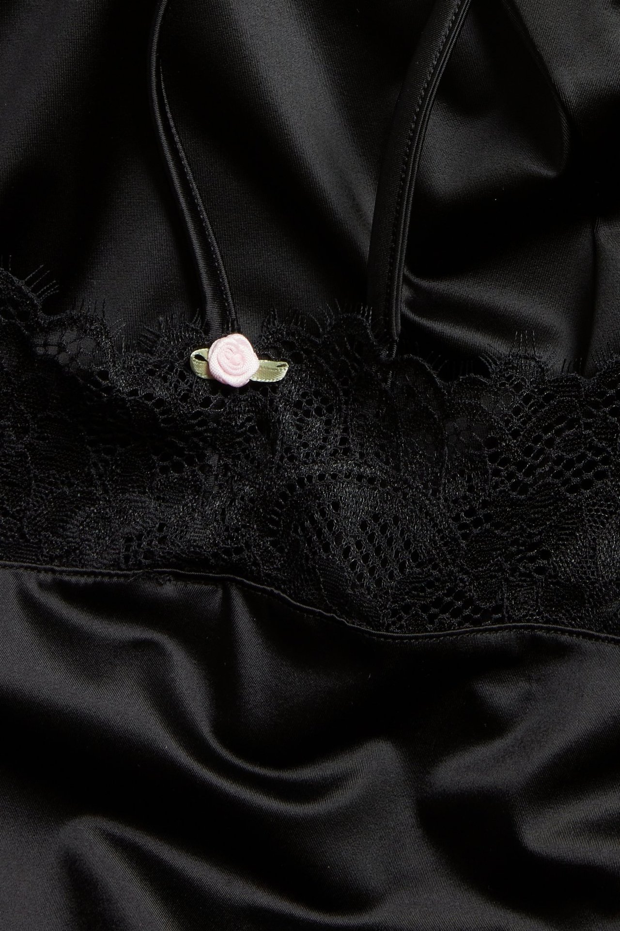 Nærbilde av en svart satengplaysuit med svart blondekant og en liten rosa rosdetalj.