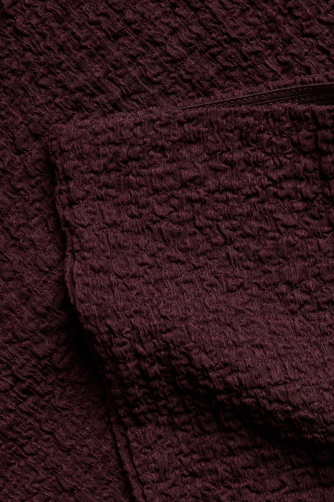 Lähikuva tummanpunaisesta, kuplakuvioisesta jerseymateriaalista, todennäköisesti pull on -housuista.