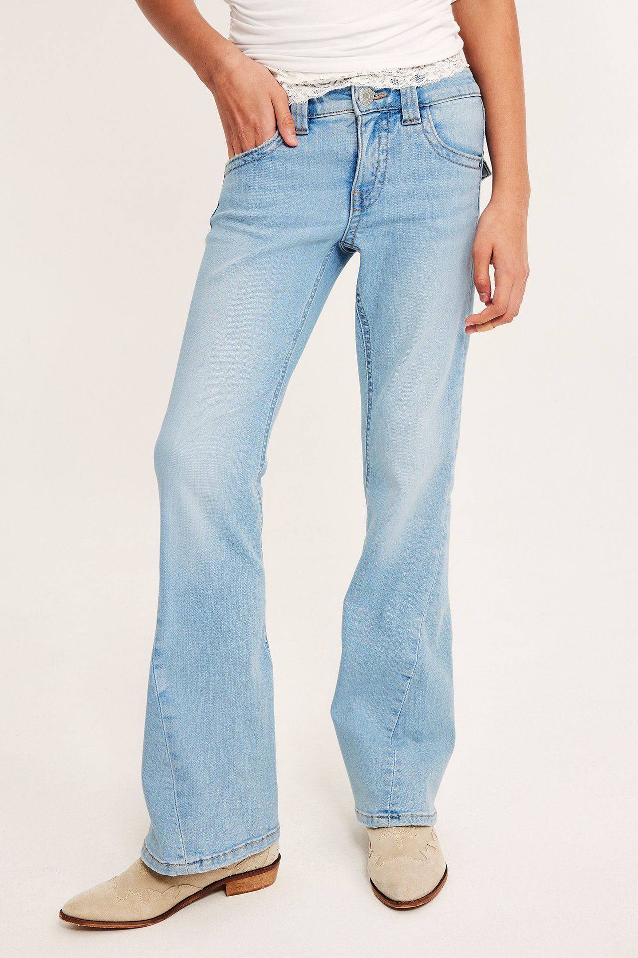 Edestäpäin: Lapsi pukeutunut vaaleansinisiin matalavyötäröisiin bootcut-farkkuihin, valkoiseen toppiin ja beigenvärisiin saappaisiin.