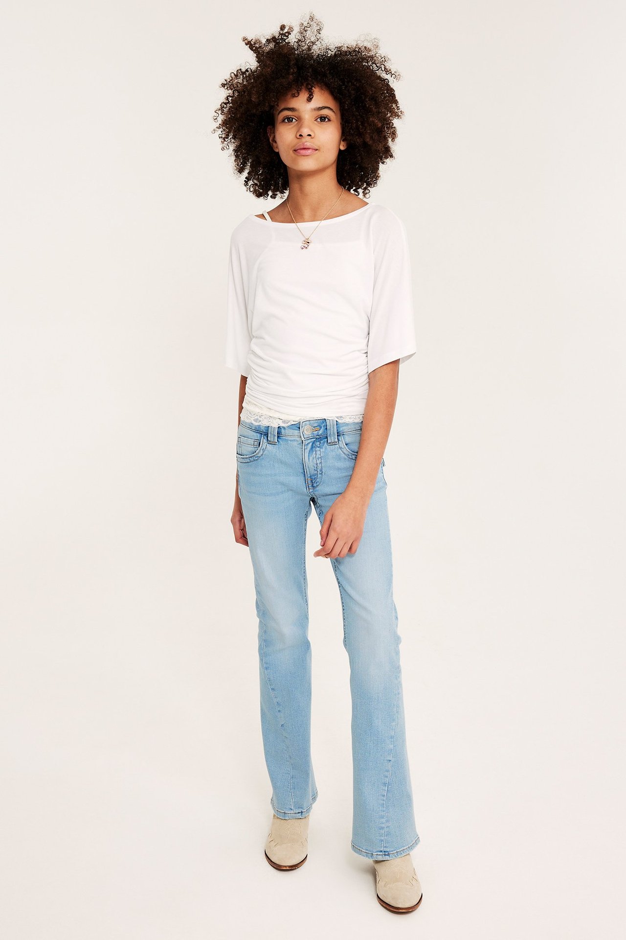 Edestä: Lapsi yllään vaaleansiniset matalavyötäröiset bootcut-farkut, valkoinen lyhythihainen toppi ja beiget nilkkurit.