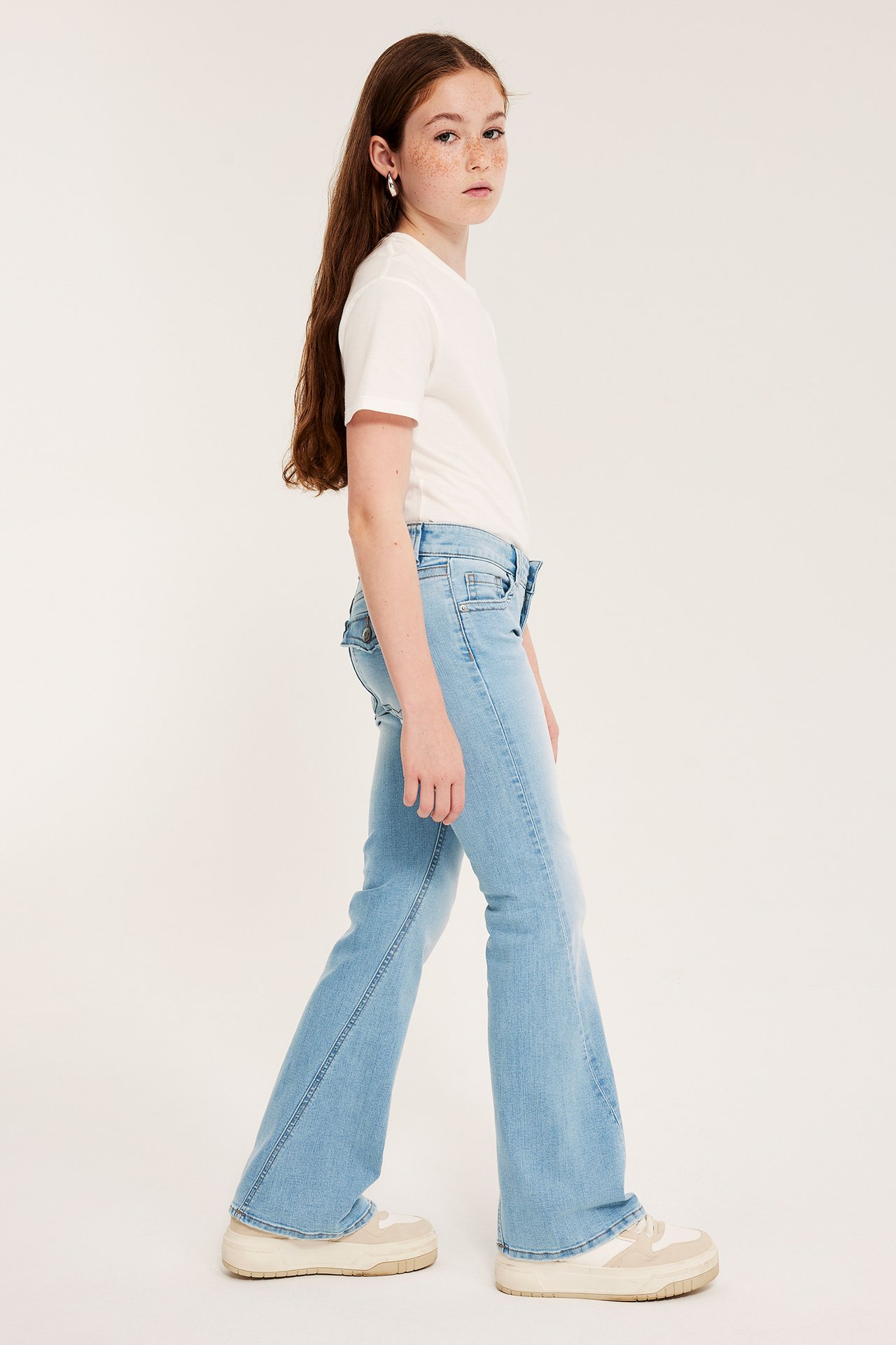 Sideutsikt: Jente iført lyseblå bootcut-jeans med lav midje, en hvit t-skjorte og platåsko.