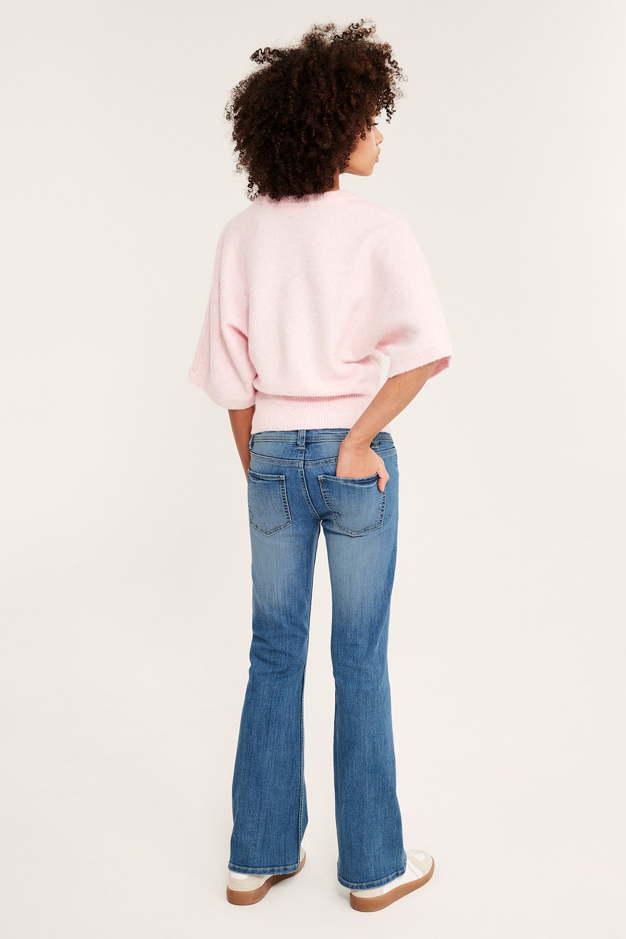 Bakfra, barn i blå denim low-waist bootcut-jeans og en lyserosa kortermet genser.