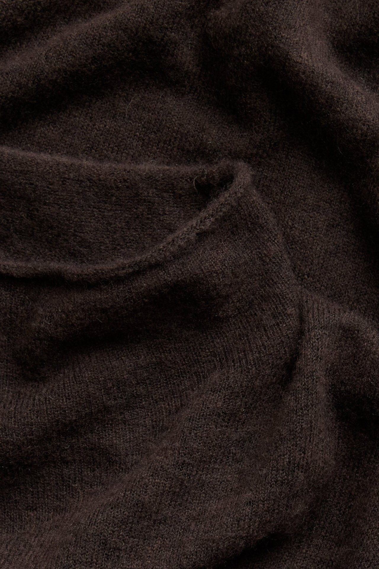 Zbliżenie złożonego, ciemnobrązowego melanżowego swetra z miękkiej mieszanki wełny.