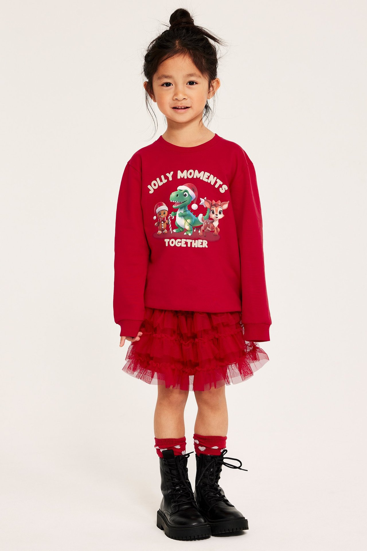 Tyttö punaisessa jouluteemaisessa collegepaidassa, punainen tylli, mustat bootsit ja sukat.