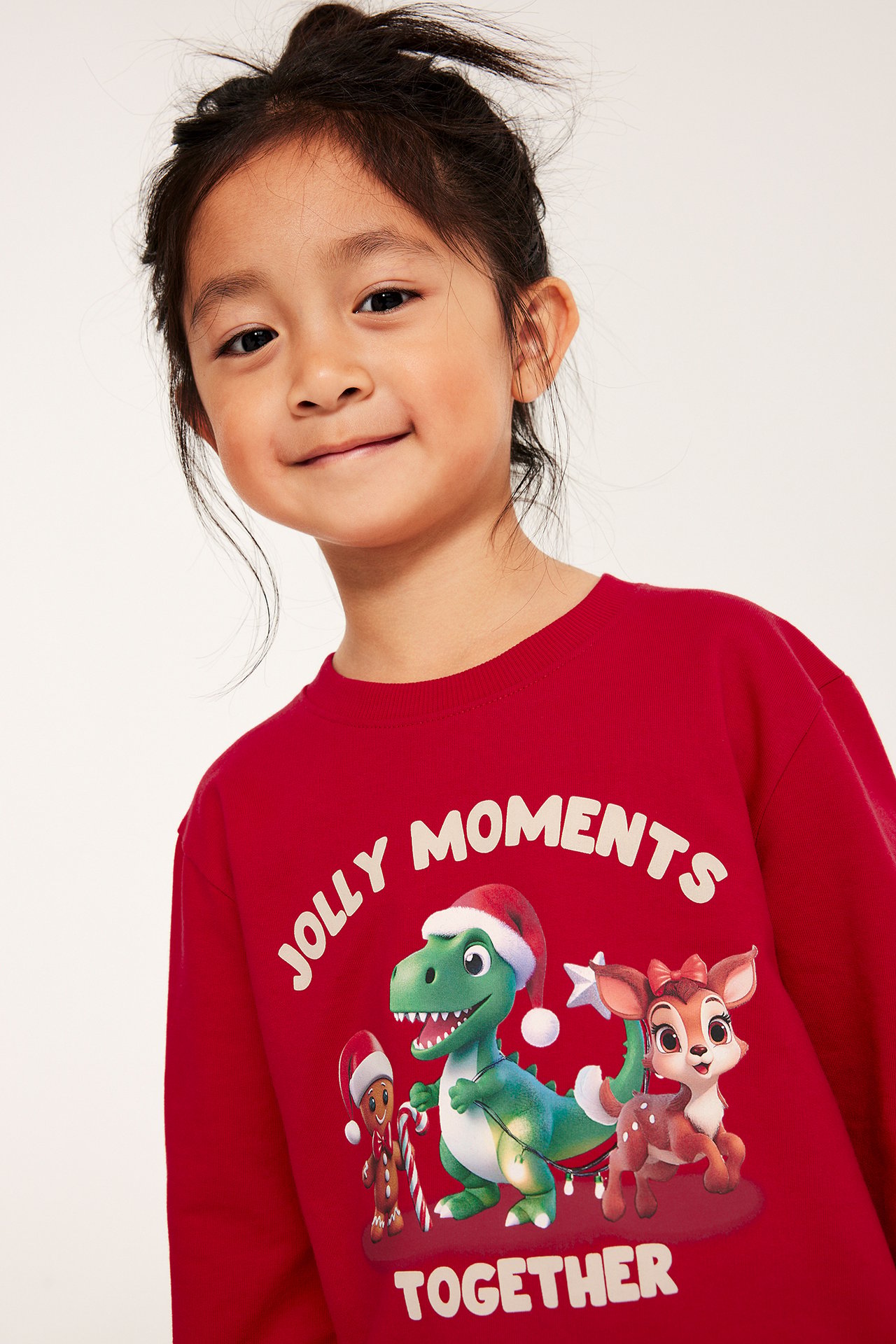 Ung kvinna i röd sweatshirt med julmotiv av dinosaurie, pepparkaksgubbe och rådjur, framifrån.