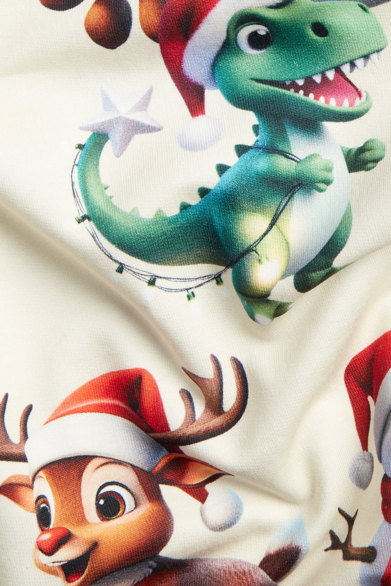 Zbliżenie na beżową, wzorzystą bawełnianą bluzę z motywem świątecznego dinozaura i renifera.