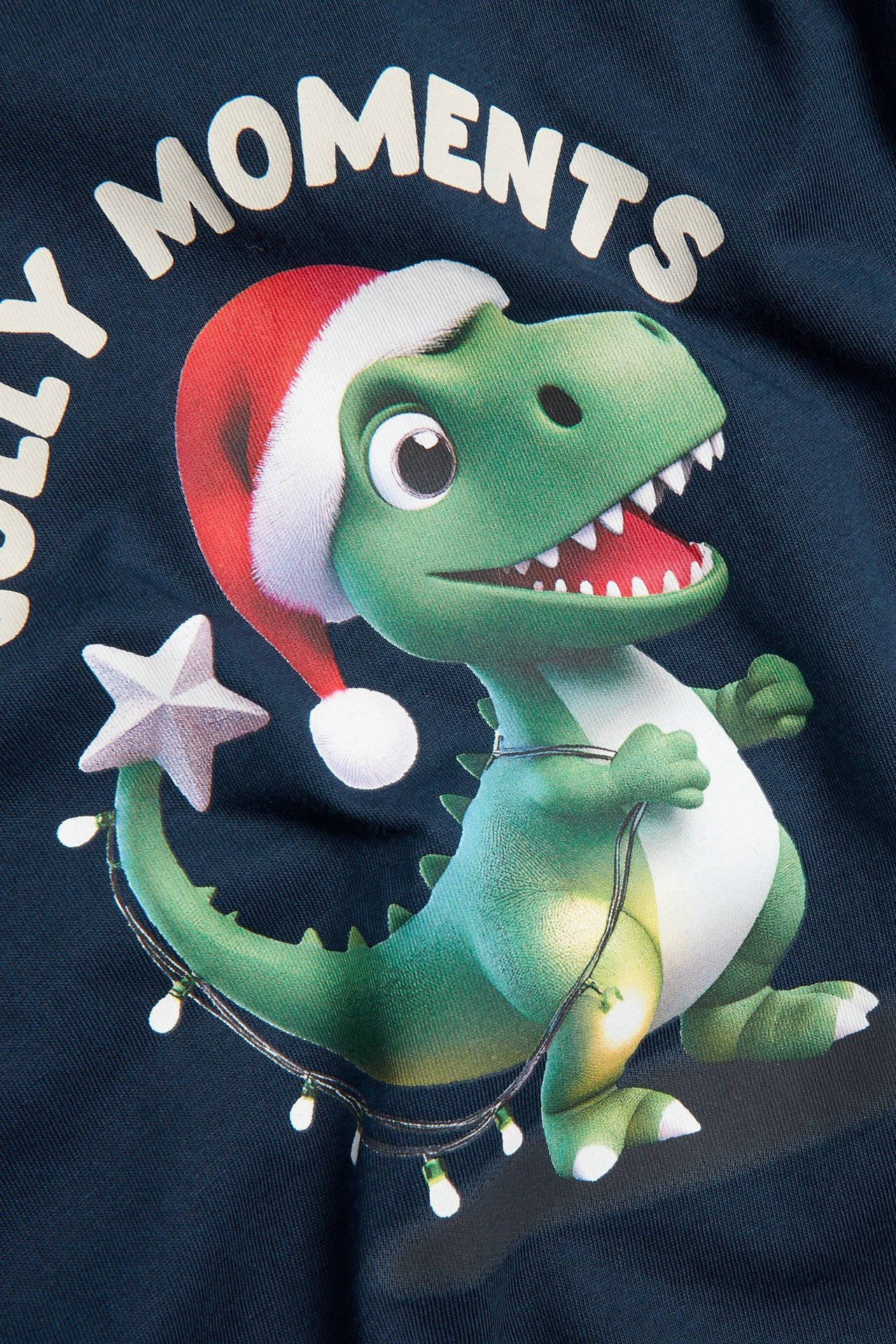 Z bliska, widok z przodu: granatowa bawełniana koszulka z zielonym dinozaurem w czapce Mikołaja i lampkami.