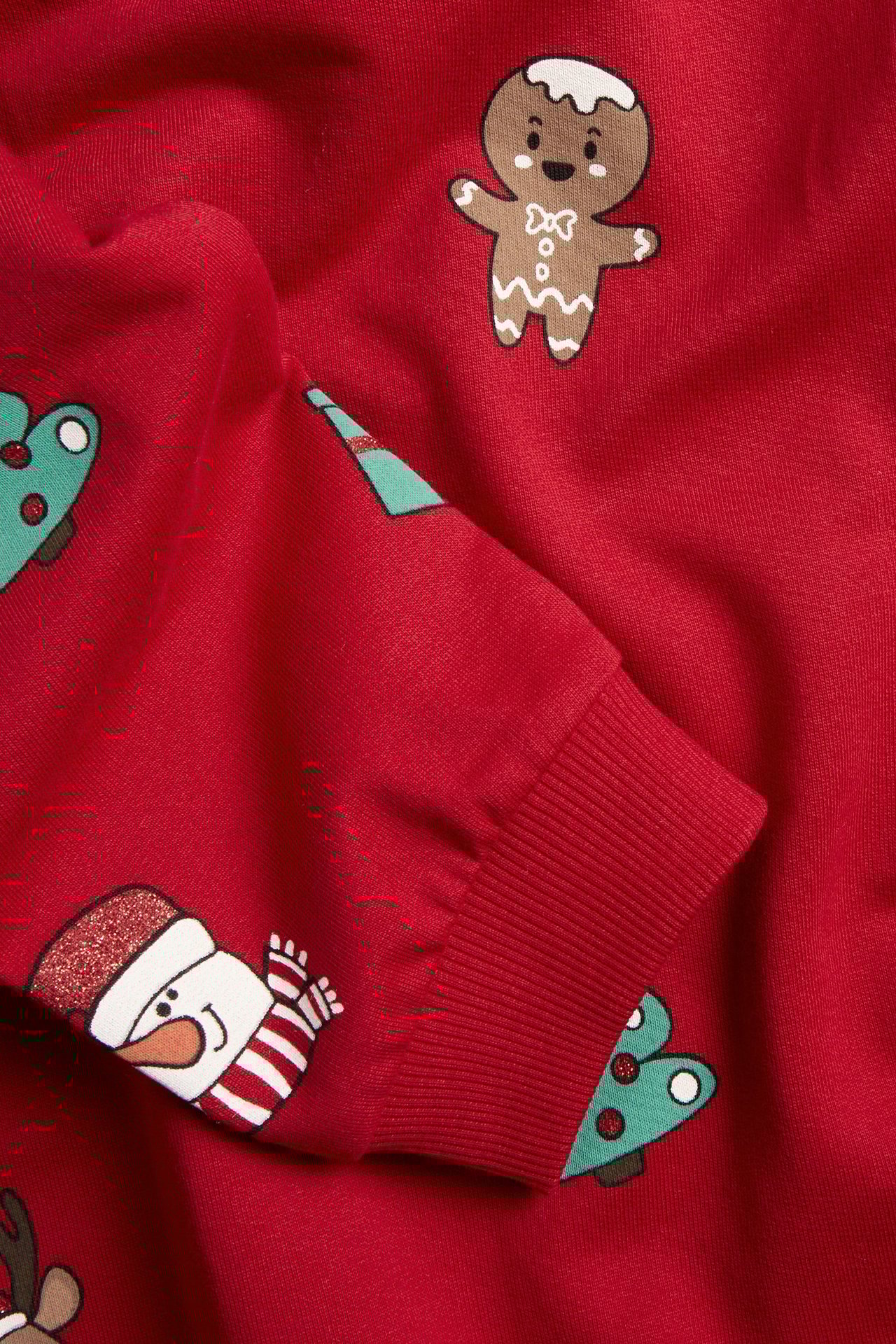Zbliżenie czerwonej bawełnianej bluzy z piernikami, bałwanami i choinkami, ściągacz na rękawie.