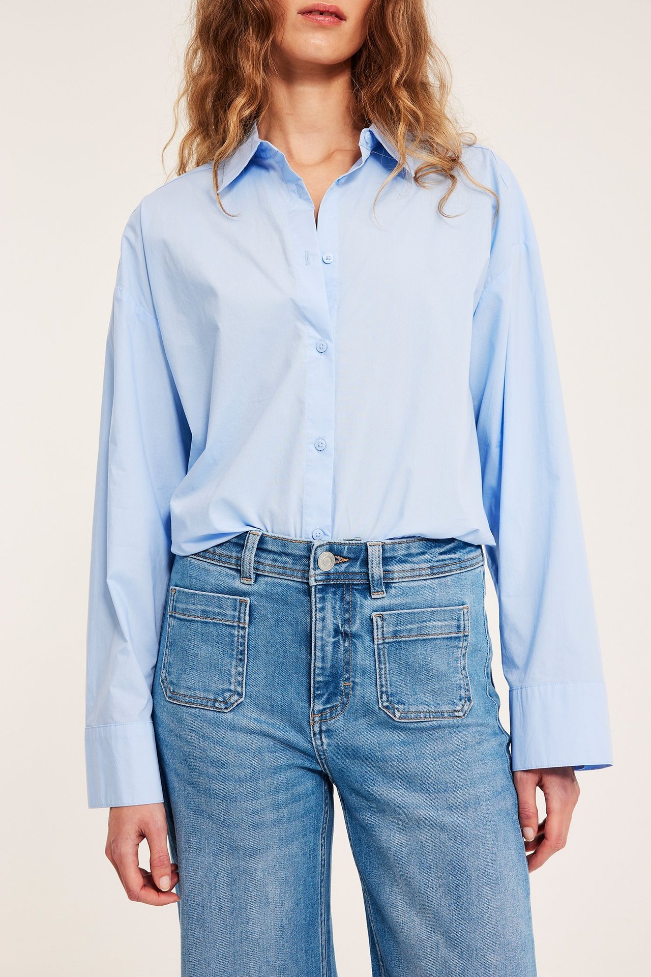 Widok z przodu: kobieta w jasnoniebieskich jeansach wide leg z wysokim stanem i jasnoniebieskiej koszuli.
