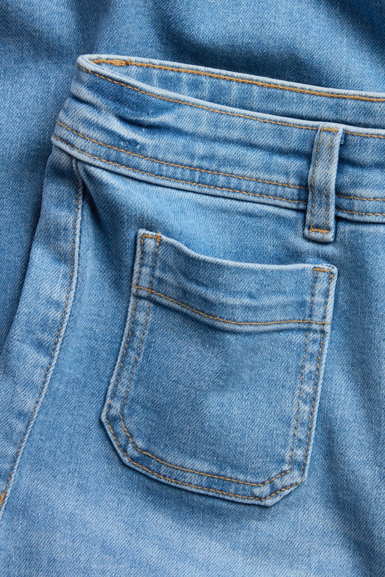 Zbliżenie jasnoniebieskich szerokich jeansów high-waist z tylną kieszenią i pomarańczowymi szwami.