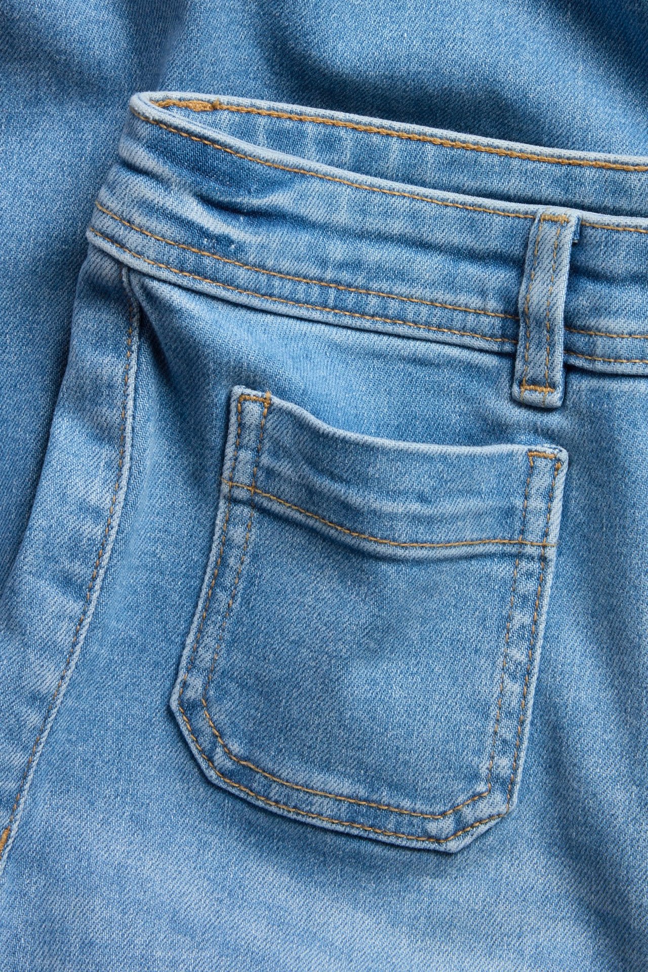 Närbild: ljusblå vida jeans med hög midja, med en utanpåficka och hällor, med kontrasterande sömmar.