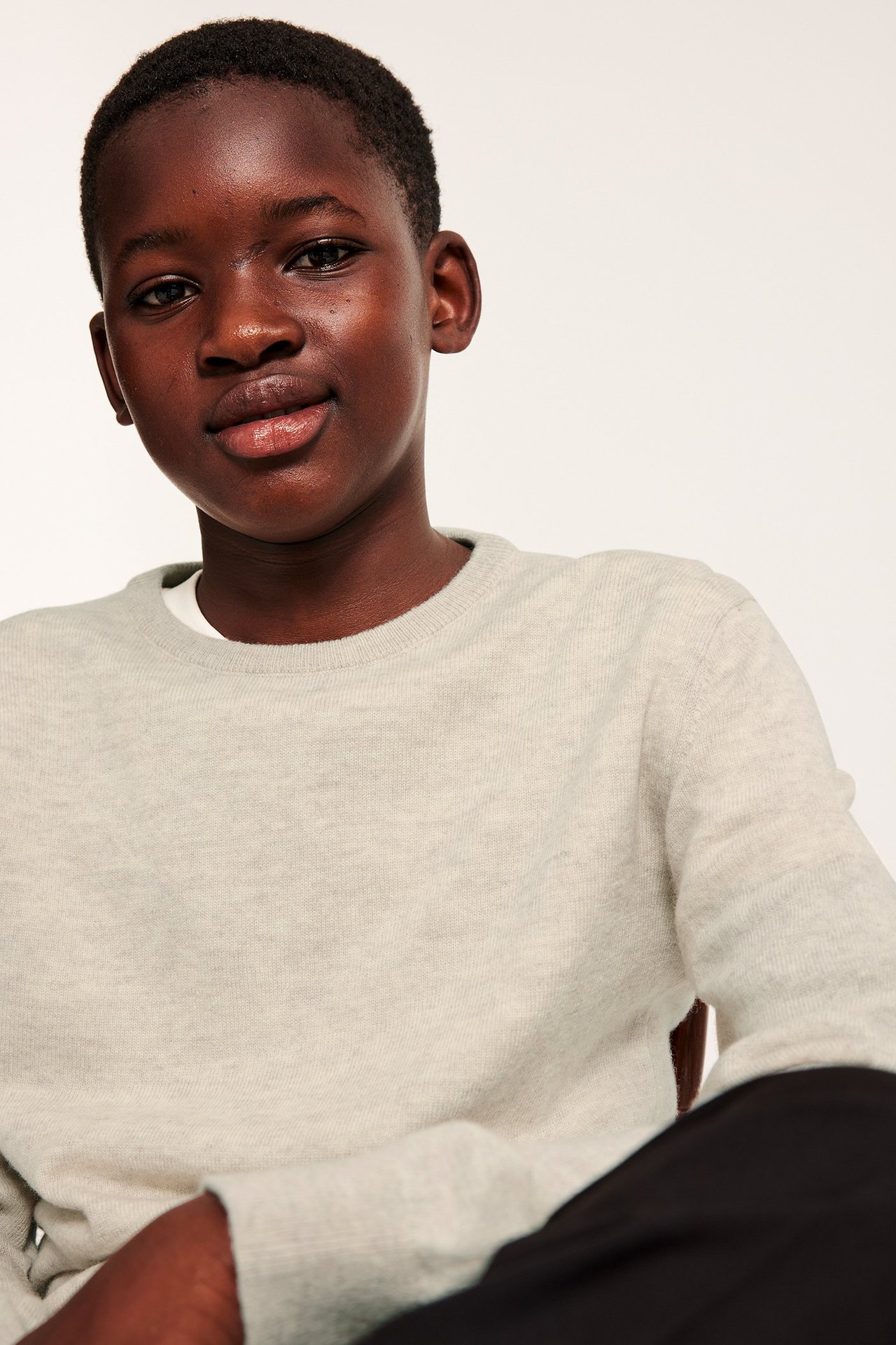 Lähikuva lapsesta beigenvärisessä meleeratussa neulotussa villapuserossa valkoisen t-paidan ja tummien housujen päällä.