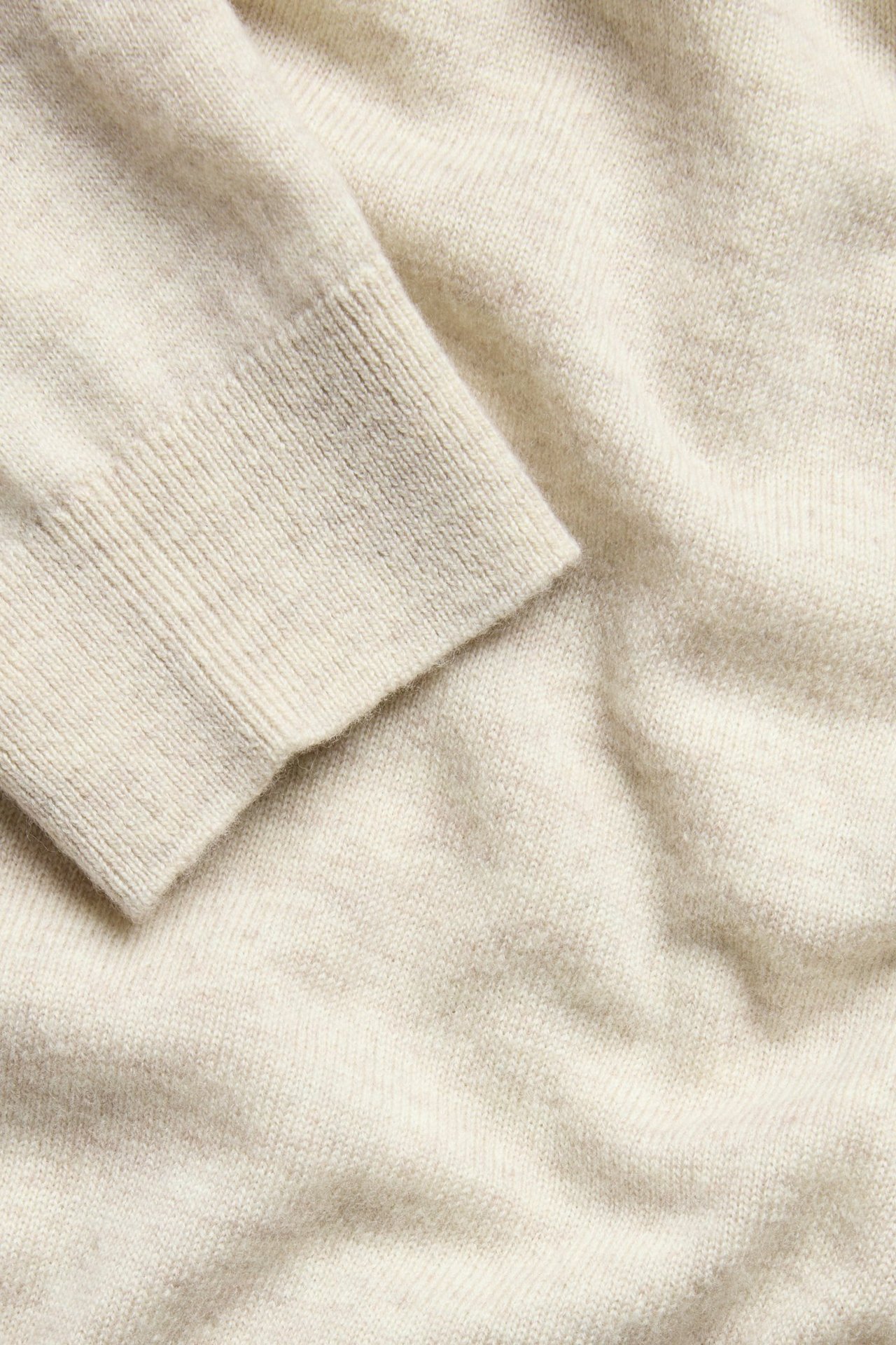 Zbliżenie beżowego melanżowego swetra z cienkiej wełny z prążkowanym mankietem.