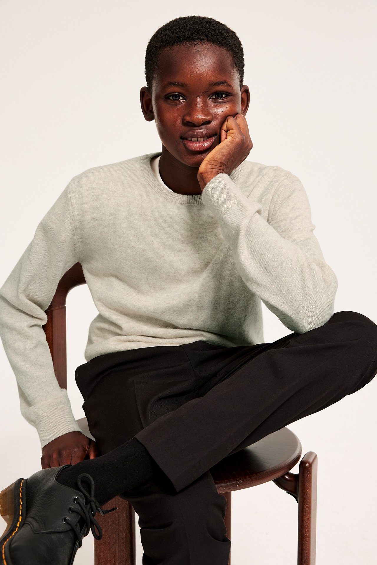 Edestä kuvattuna lapsi yllään beigenvärinen kirjava hienoneulottu villapusero, mustat housut ja mustat nauhakengät.