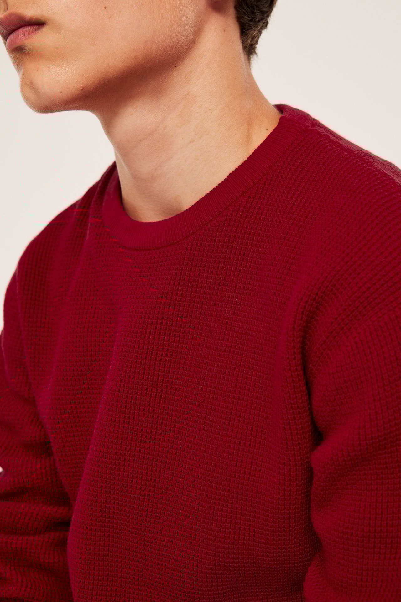 Lähikuva miehestä yllään punainen neulepusero vohvelikuviolla ja ribbireunoilla.