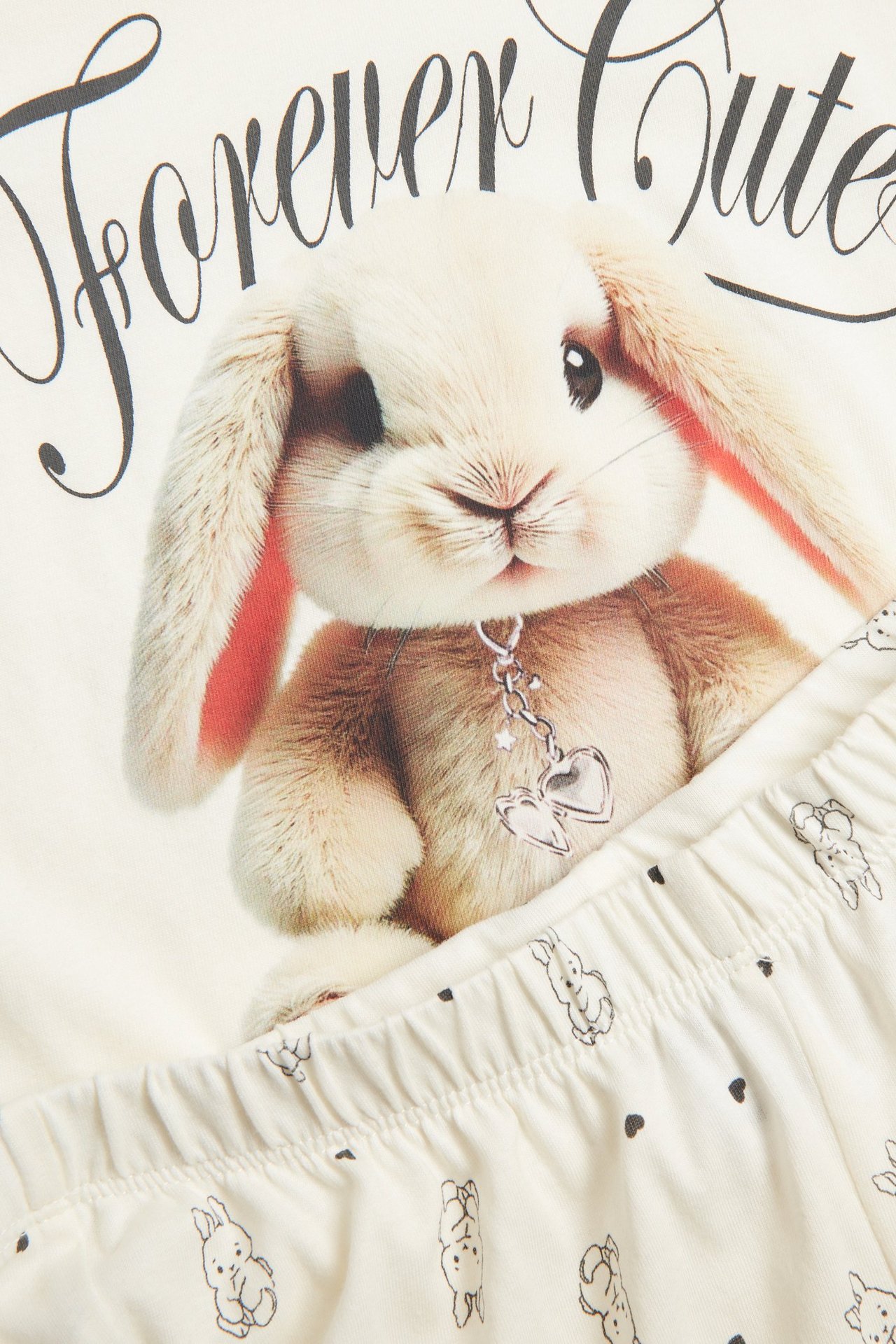 Zbliżenie na dziecięcą bawełnianą piżamę ecru z dużym nadrukiem królika na górze i małymi króliczkami na dole.