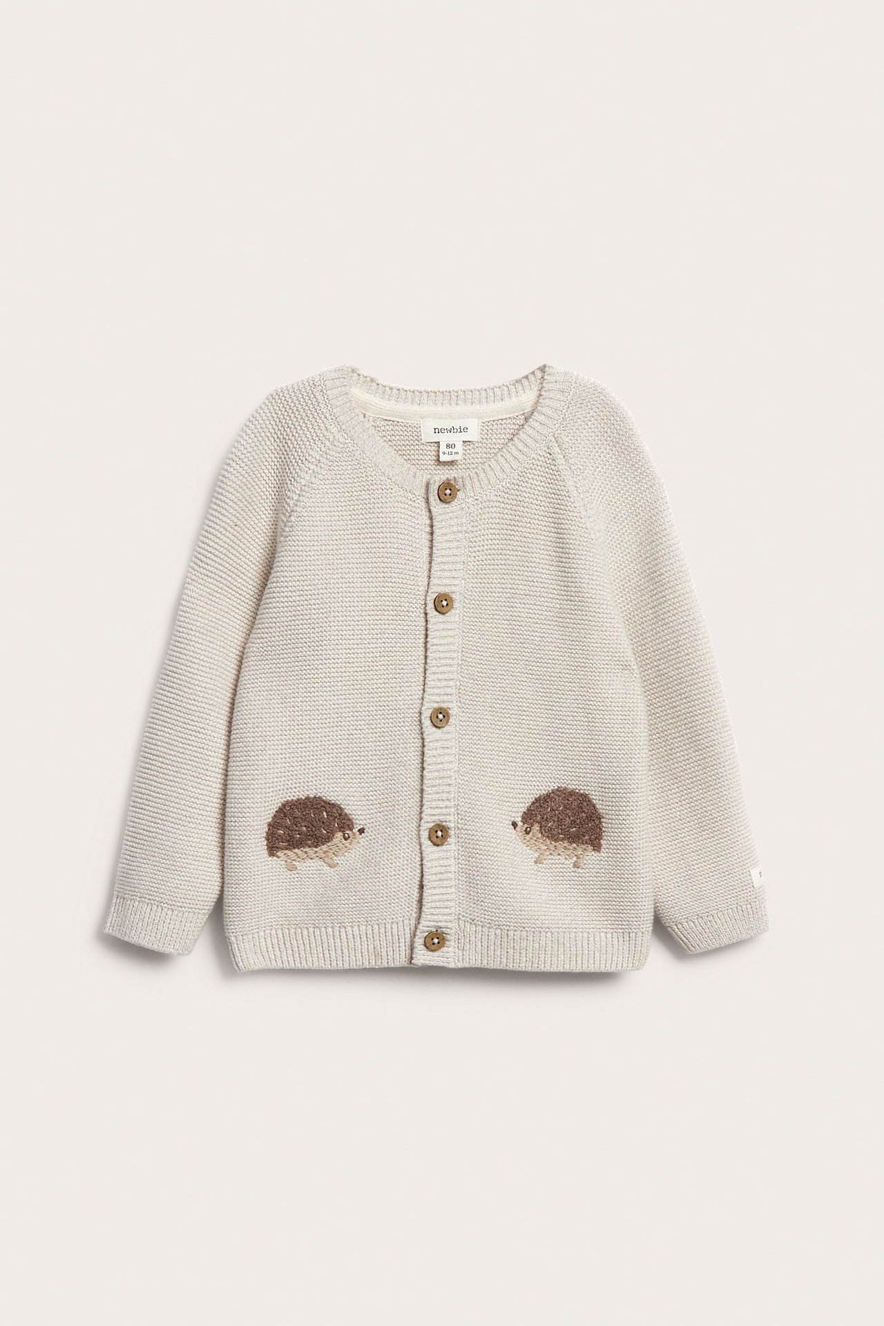 Frontvisning av en beige melert strikket babycardigan med fem knapper og myke pinnsvinbroderier.