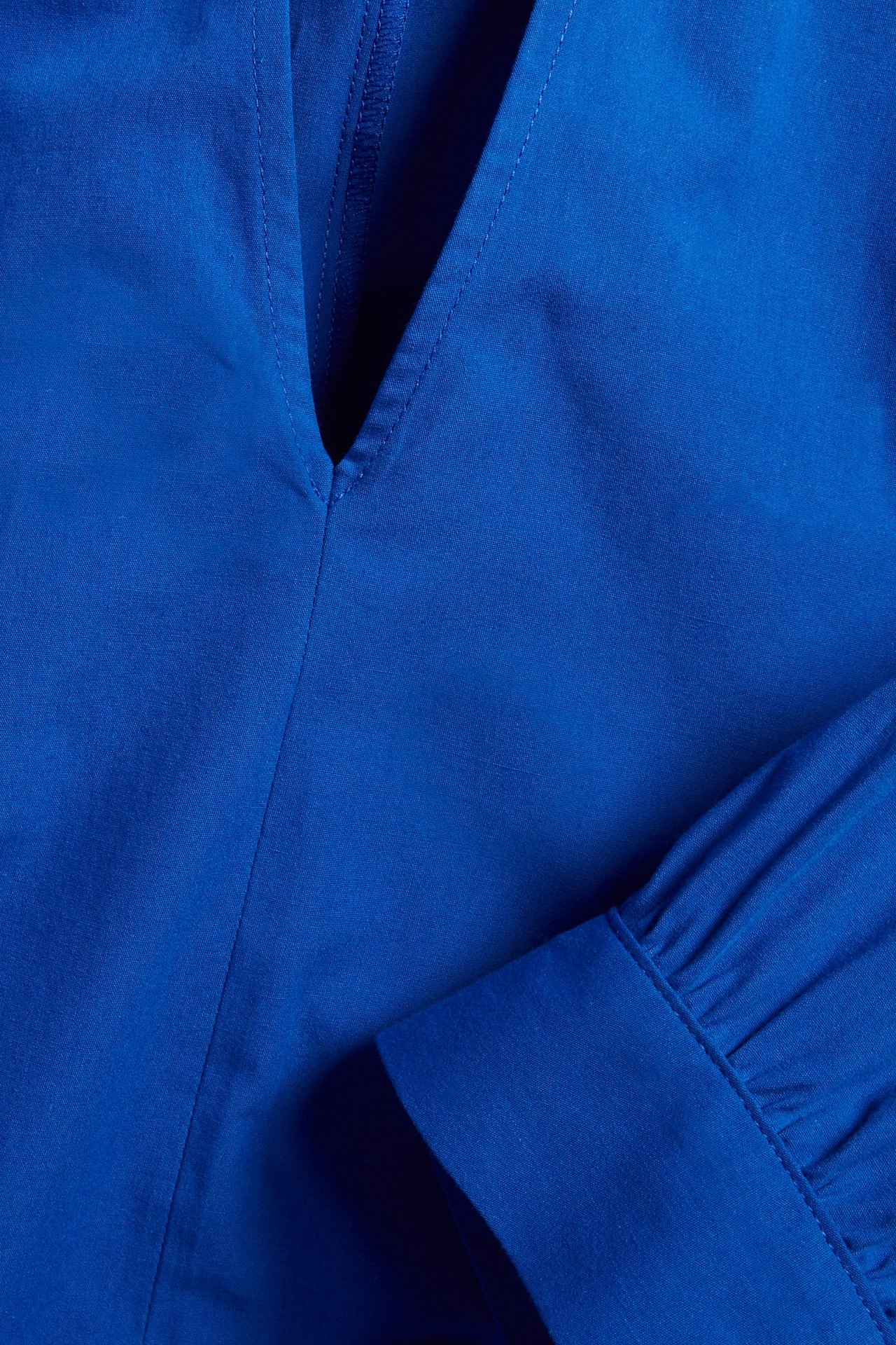 Zbliżenie niebieskiej krótkiej sukienki z bawełnianej popeliny z dekoltem w serek i marszczonym mankietem.