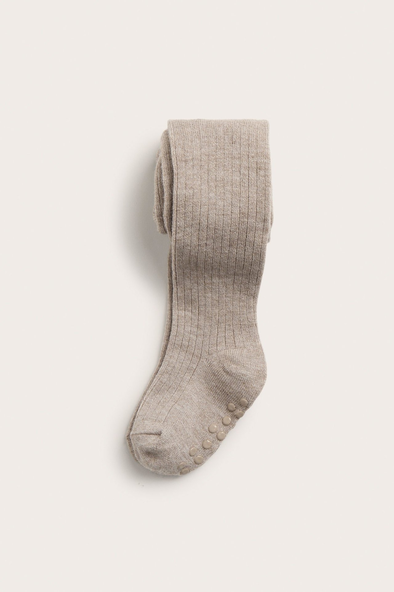 Frontvisning av brettede beige ribbestrikkede ullblandingsstrømpebukser for baby med antiskli-knotter.